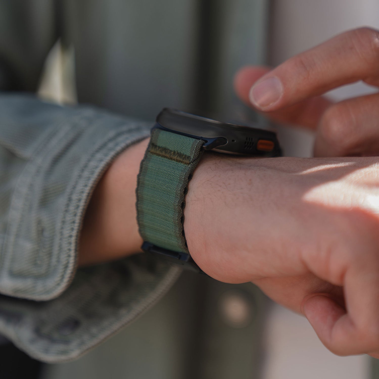 Jemand berührt den Bildschirm seiner Apple Watch, während er das arktisband Apple Watch Armband "CoreX" aus grünem Stoff mit einem Fallschirm-Verschluss von arktisband trägt.