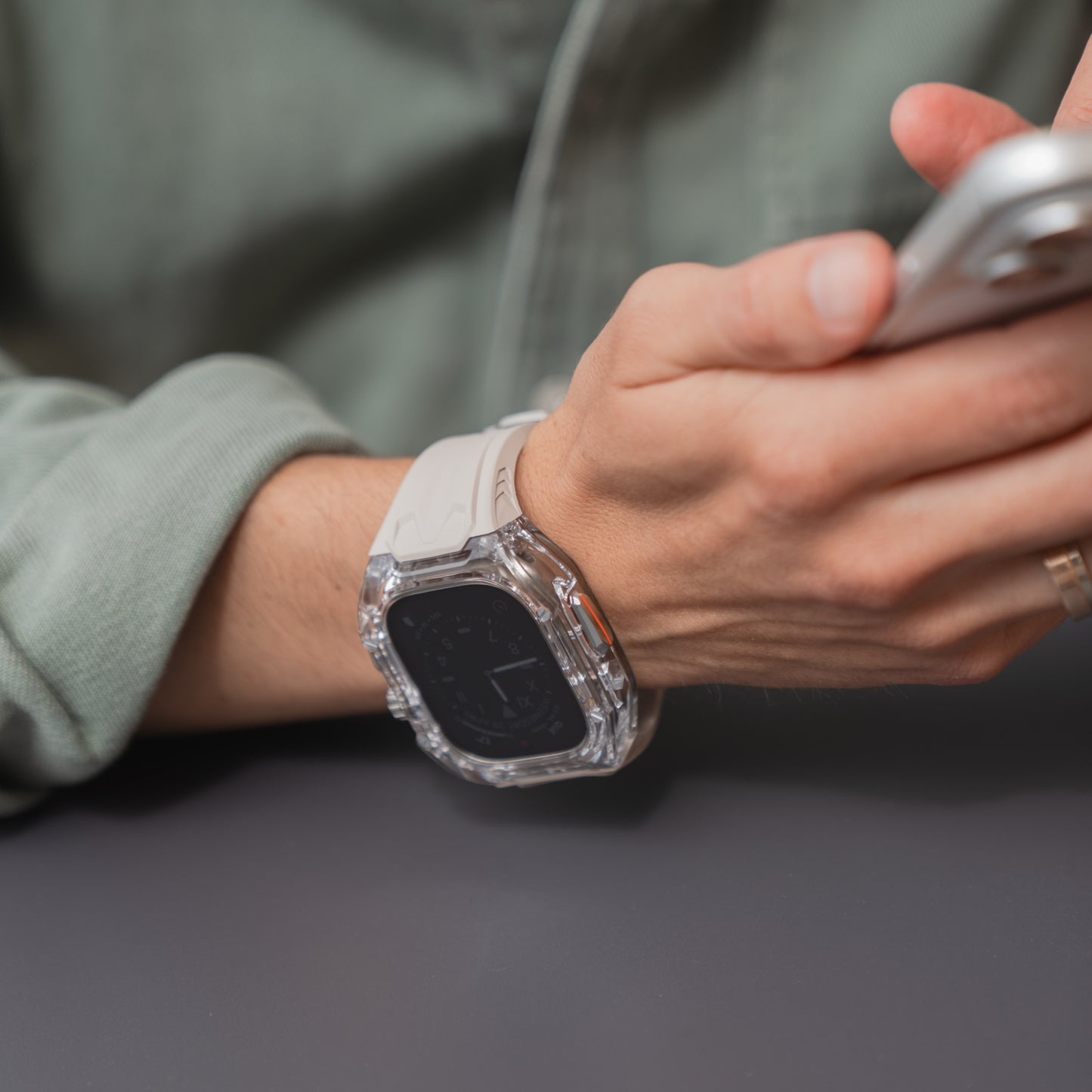 Eine Person, die ein arktisband Apple Watch Armband "Armor Fusion" von arktisband trägt und ein Smartphone mit einem transparenten Hardcase hält, sitzt an einem Tisch.