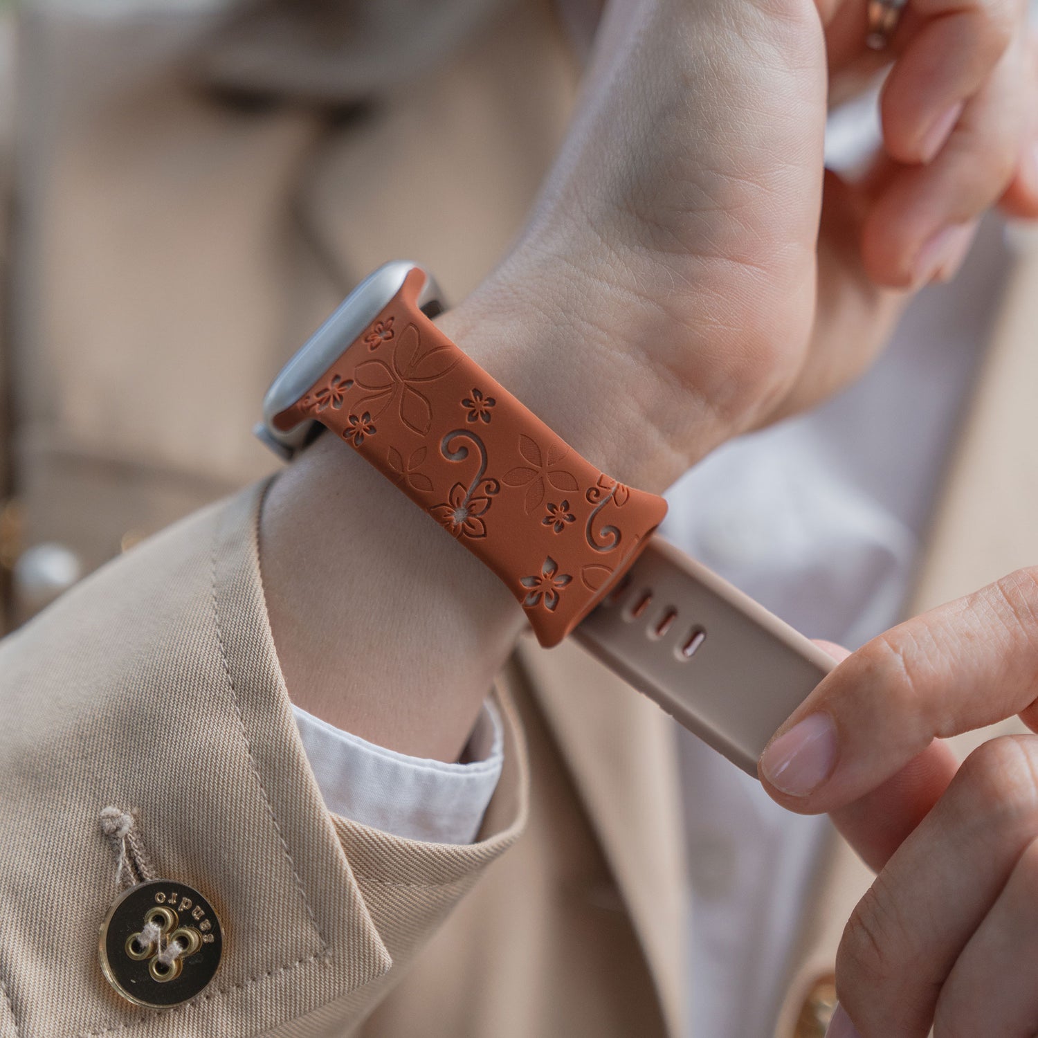 Eine Person befestigt ein arktisband Apple Watch Silikonarmband "Bloom", ein floral gemustertes braunes Silikonarmband von arktisband, an ihrem Handgelenk.