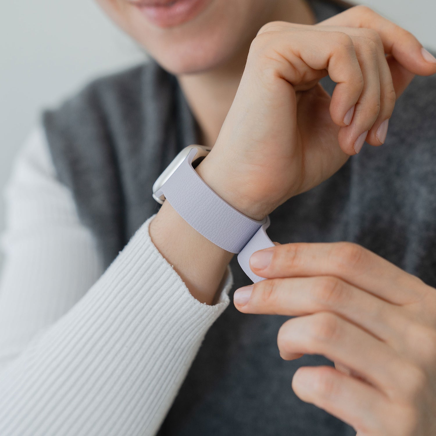 Eine Person passt das magnetische Silikonarmband "Flexy" der Apple Watch an ihrem Handgelenk an, während sie ein weiß-graues langärmeliges Outfit trägt.