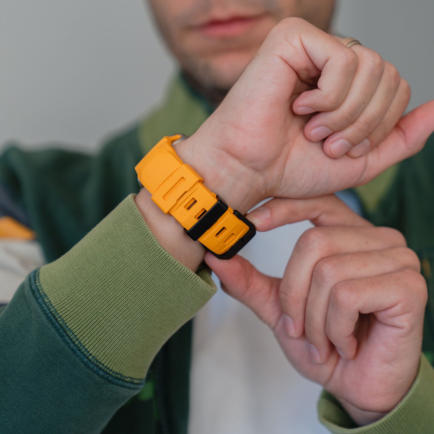 Eine Person passt ein arktisband Apple Watch Armband "Flux" mit Edelstahl Schließe an ihr Handgelenk an, während sie eine grüne Jacke trägt.