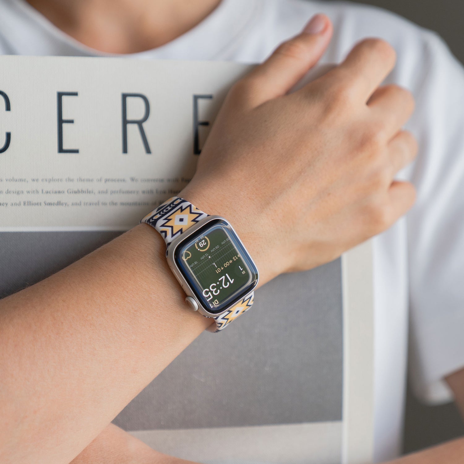 Eine Person trägt ein arktisband Aztec Apple Watch Armband von arktisband und hält eine Zeitschrift mit CERE auf dem Cover.