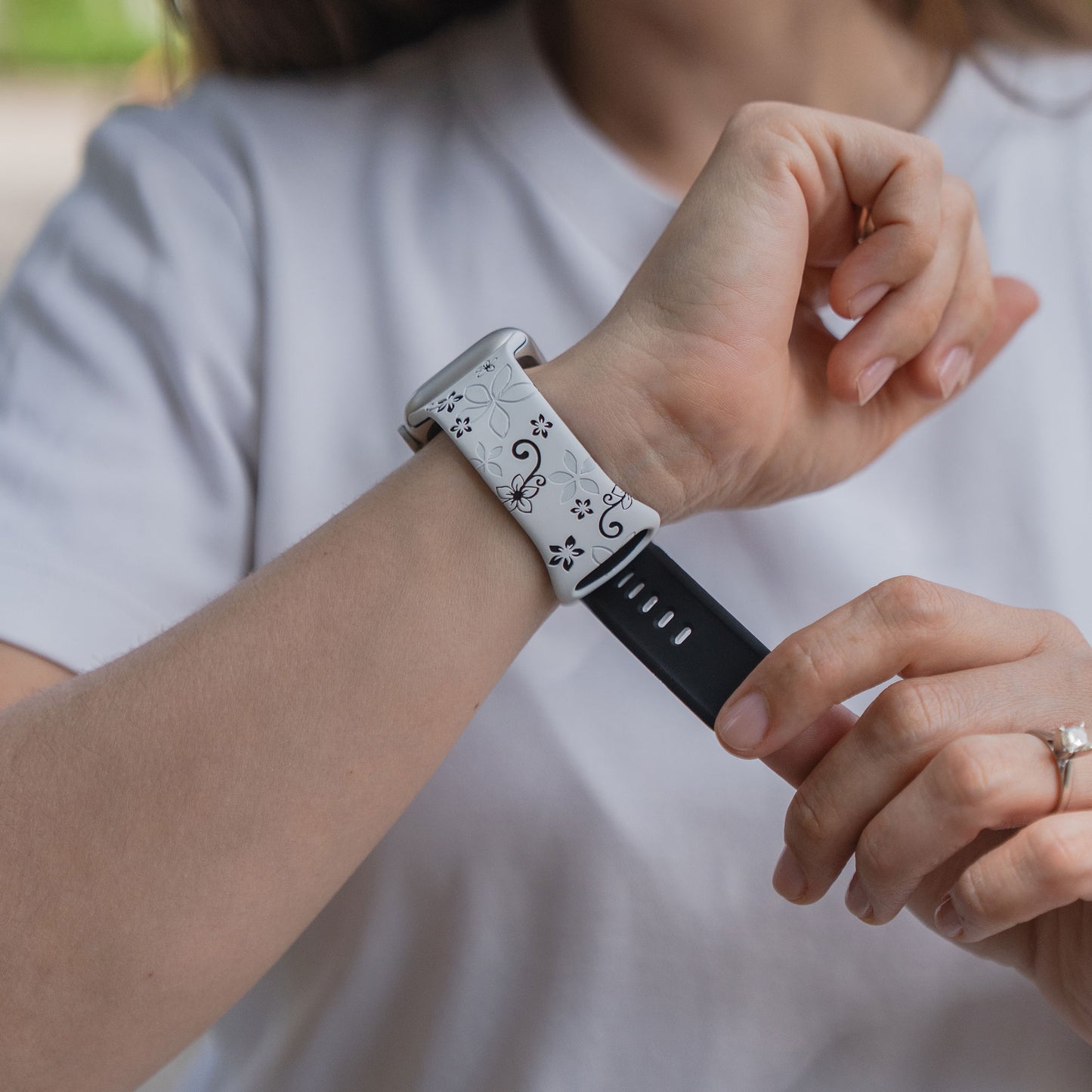 Eine Person in einem weißen Hemd passt ein arktisband Apple Watch Silikonarmband "Bloom" an ihr Handgelenk an, ein florales Silikonarmband von arktisband, das mit der Apple Watch kompatibel ist.
