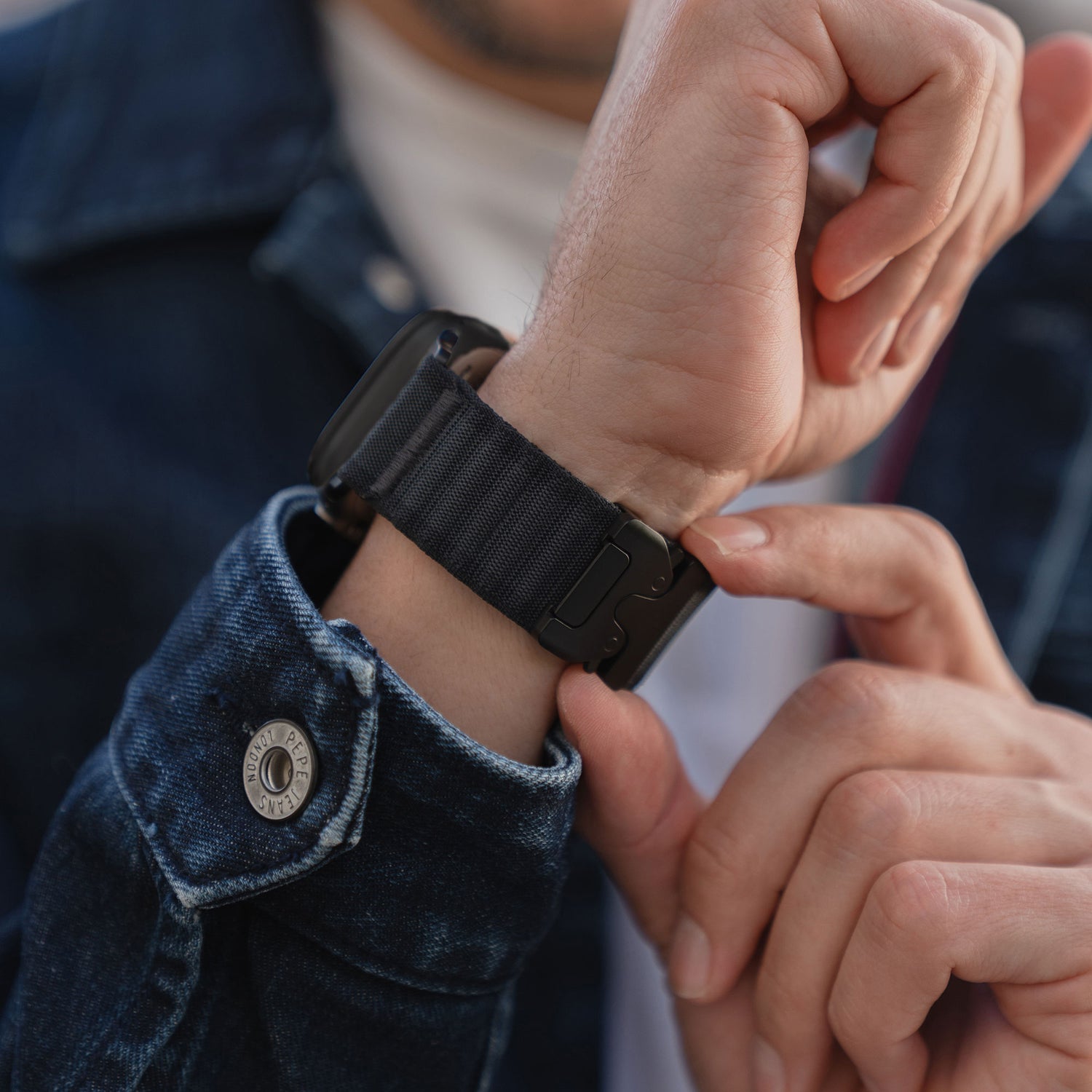 Eine Person, die das schwarze arktisband Apple Watch Armband "CoreX" von arktisband an ihrem Handgelenk befestigt und eine Jeansjacke trägt.