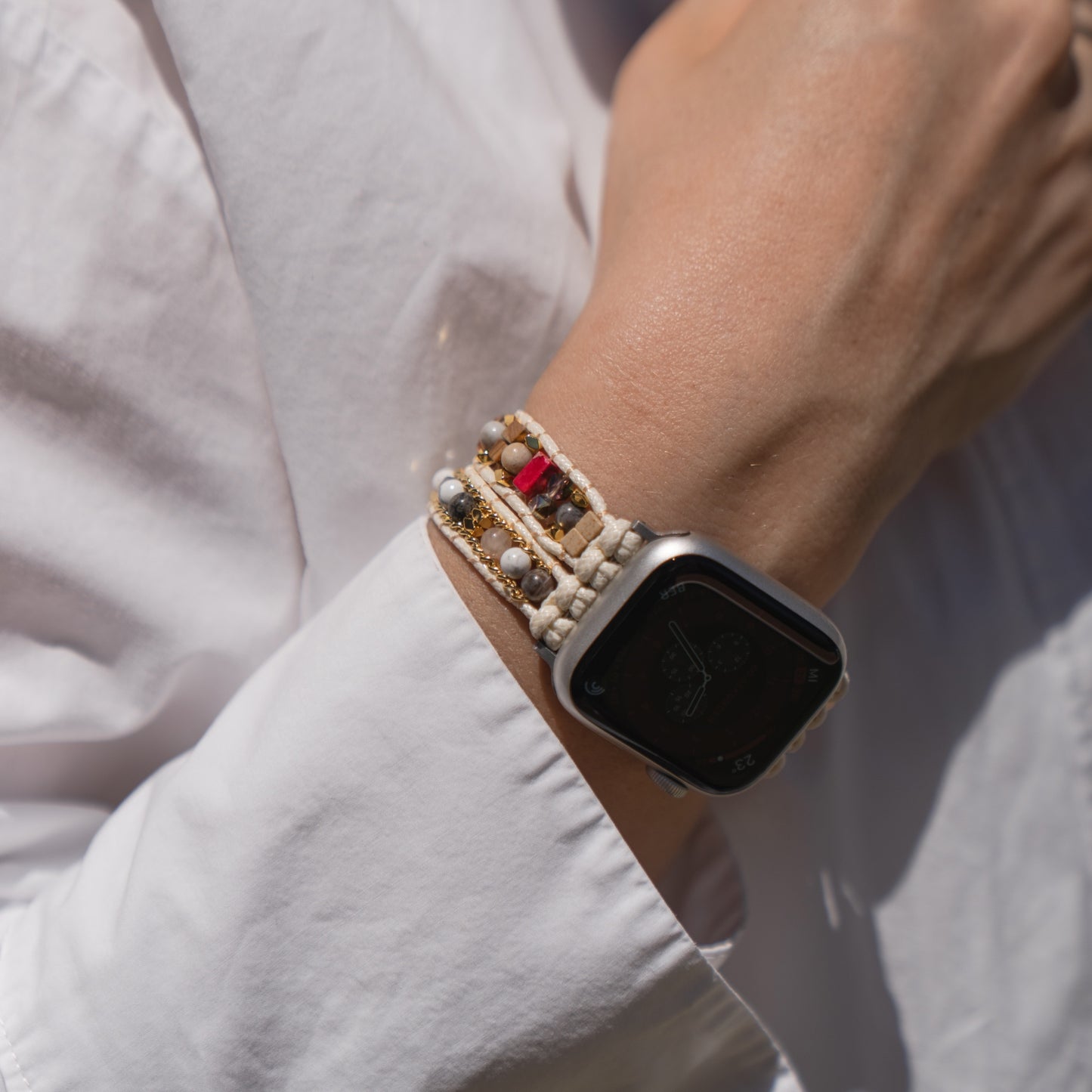 Eine Person, die das Arktisband Apple Watch-Armband „Sunset Spirit“ und ein Perlenarmband am Handgelenk trägt und ein weißes Hemd trägt.