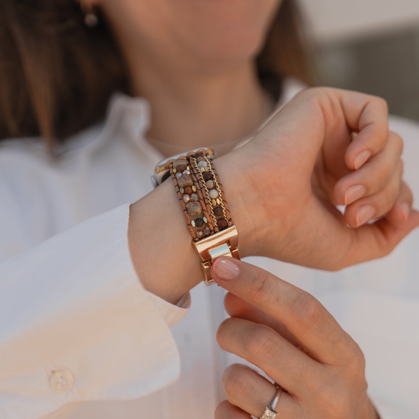 Eine Frau in einem weißen Hemd legt das arktisband Apple Watch-Armband „Sunset Spirit“ an ihrem Handgelenk zurecht und präsentiert das stilvolle Accessoire von arktisband mit ihren gepflegten Händen.