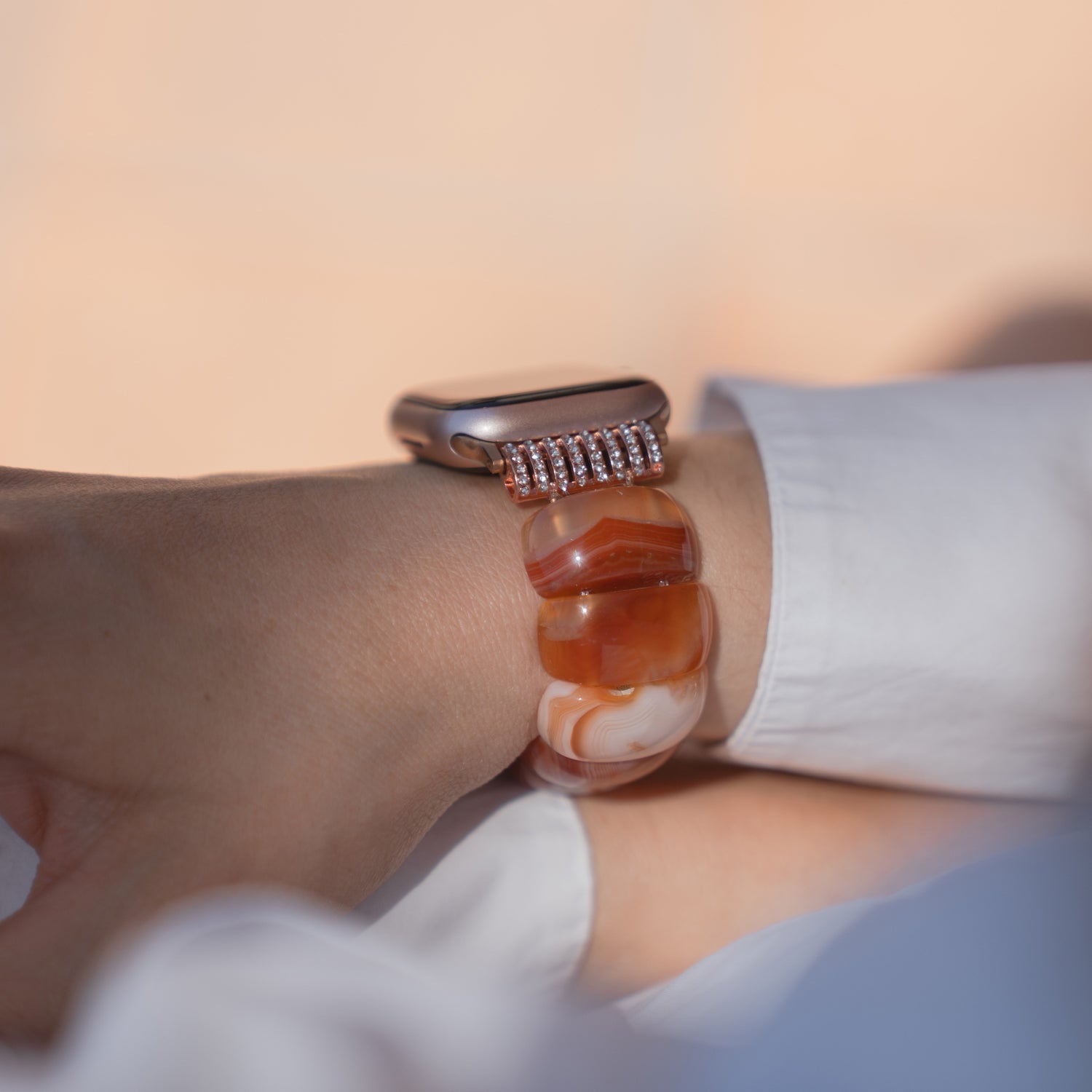 Am Handgelenk befindet sich eine Apple Watch „Stone Pearl“ von arktisband mit einem orange-weißen Naturstein-Armband, dazu ein strahlend weißer Ärmel.