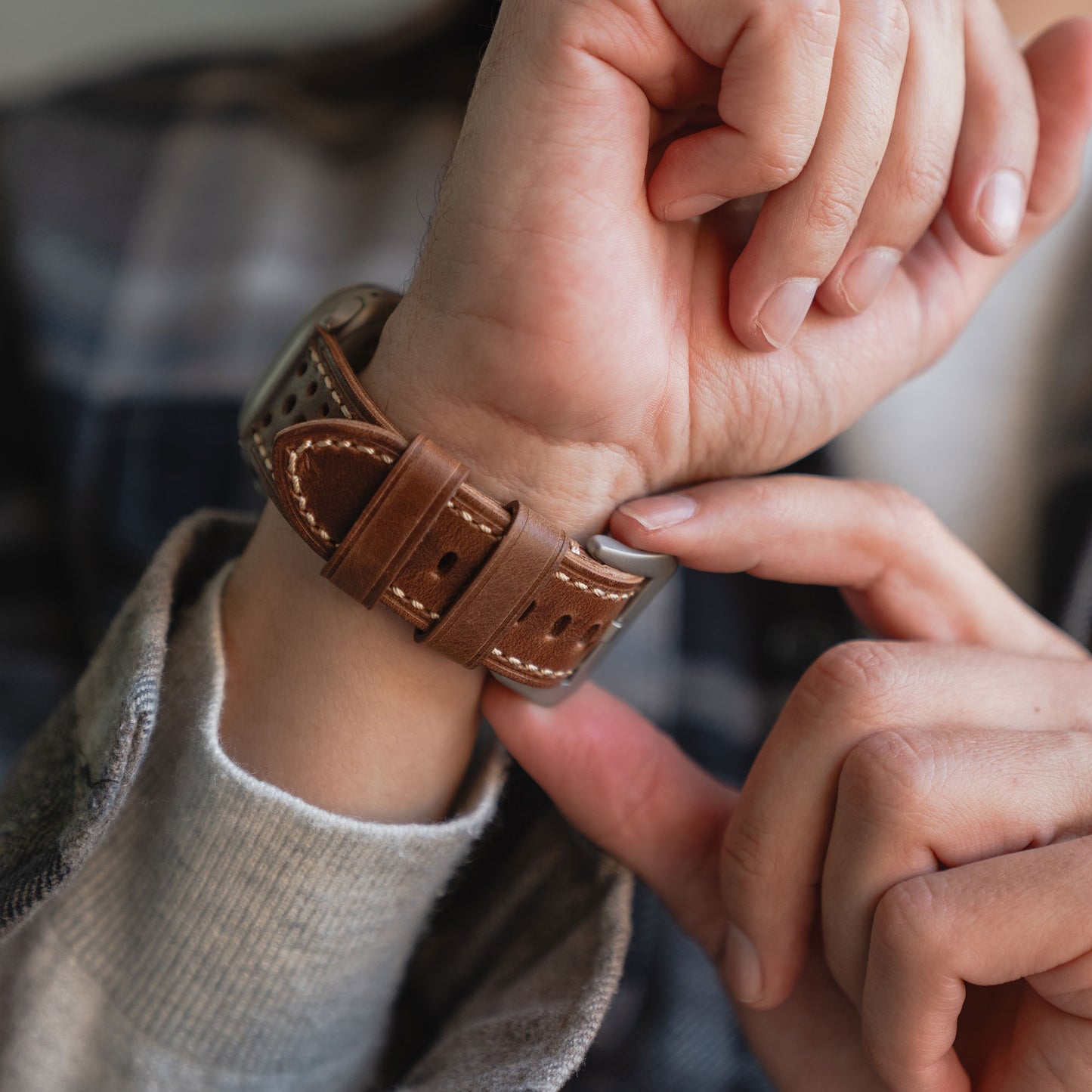 Jemand passt ein arktisband Apple Watch Lederarmband "Toronto" an seinem Handgelenk an, während er ein grau kariertes Hemd trägt.