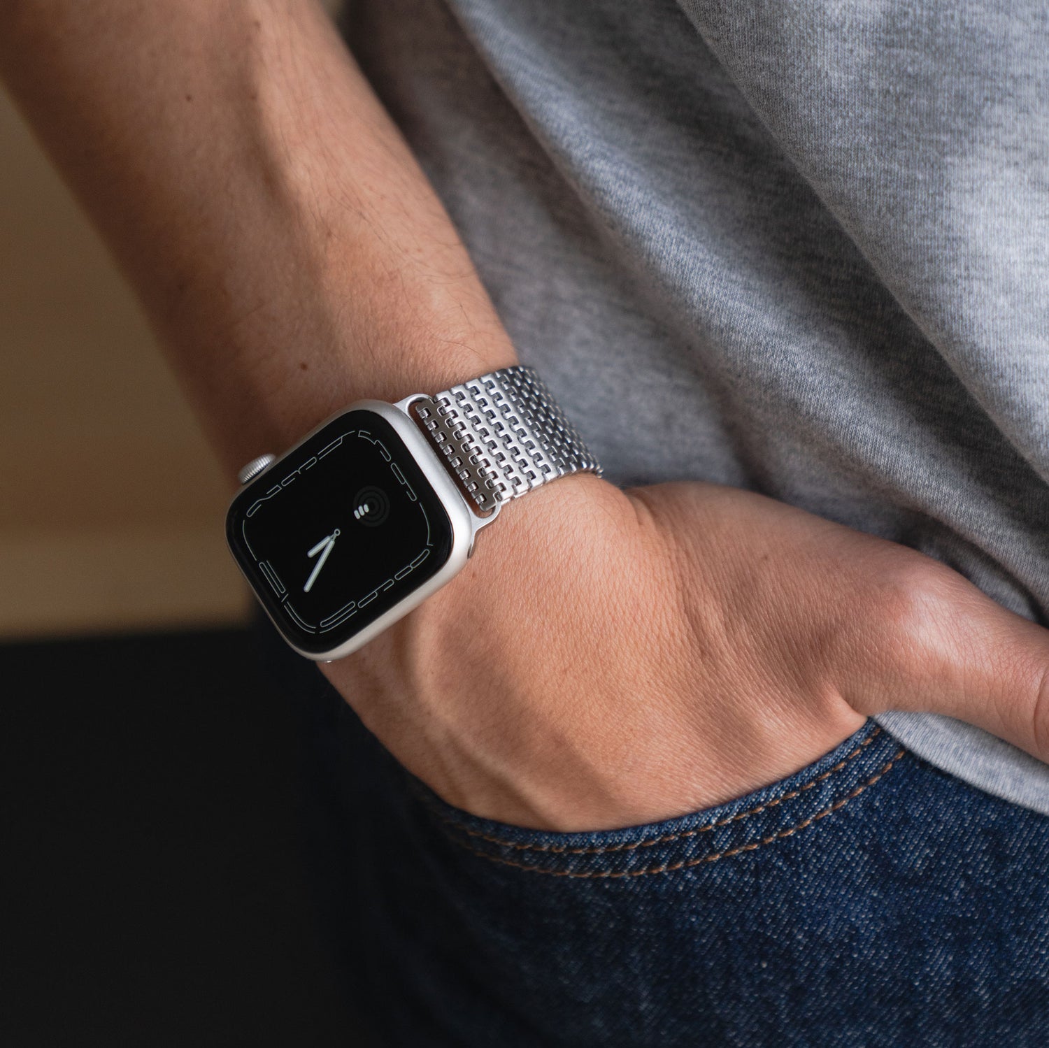 Eine Person trägt ein Arktisband Apple Watch Edelstahlarmband „Aurora“ mit Magnetverschluss und ein graues Hemd, die Hand in der Tasche einer Bluejeans.