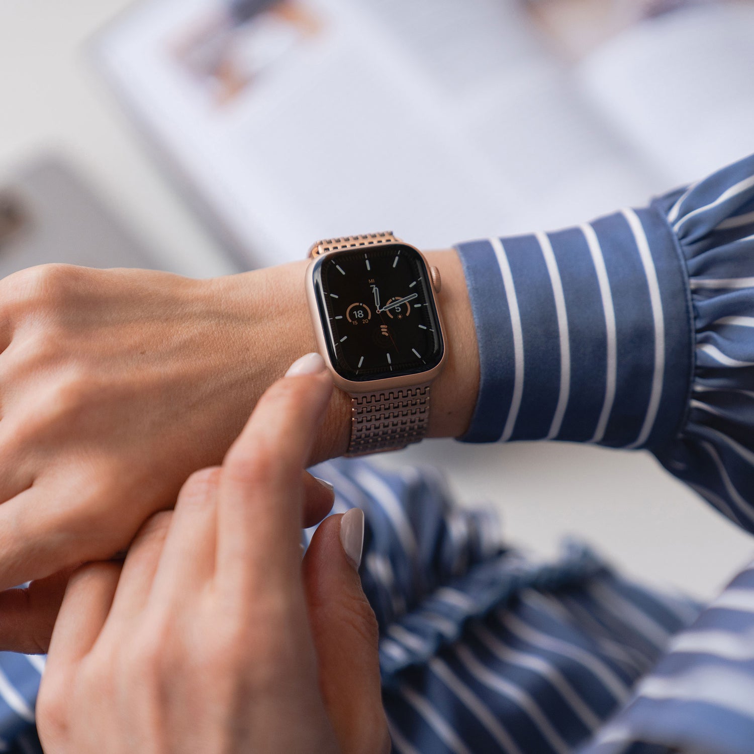 Eine Person in einem gestreiften Hemd überprüft die Uhrzeit auf einem Arktisband Apple Watch Edelstahlarmband „Aurora“ mit einem eleganten Magnetverschluss.