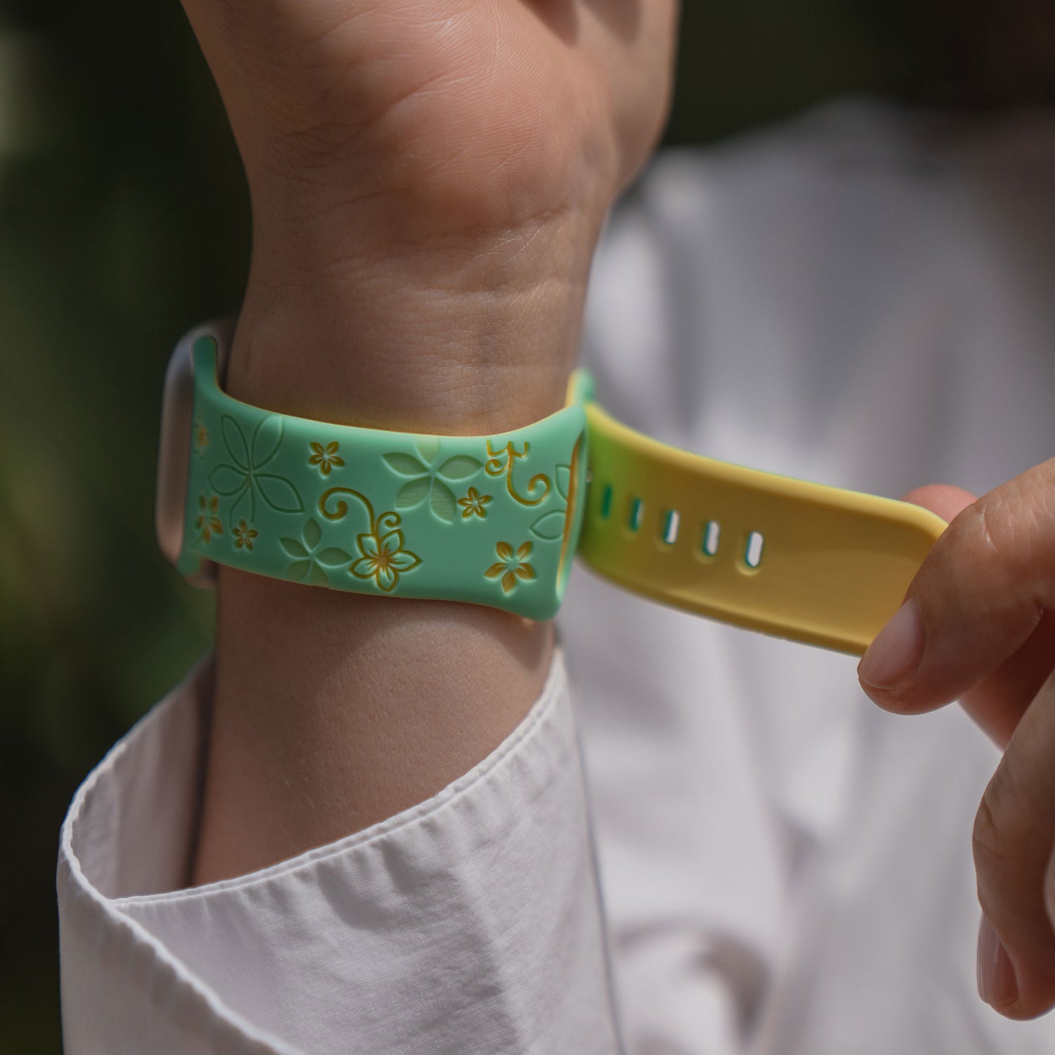 Eine Person, die ein weißes Hemd trägt, befestigt das arktisband Apple Watch Silikonarmband "Bloom", ein gelbes und grünes Blumenarmband von arktisband, an ihrem Handgelenk.