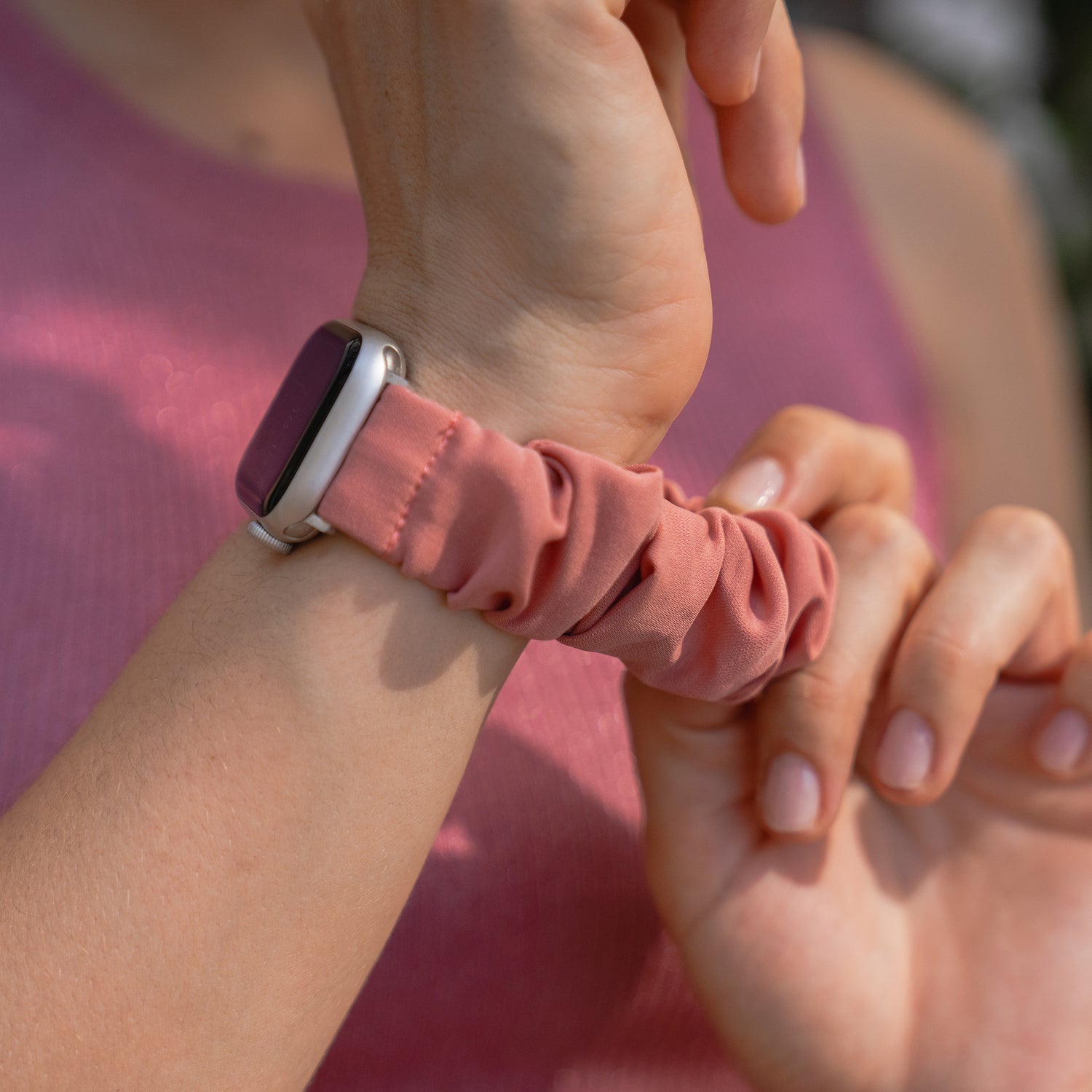 Nahaufnahme einer Person, die das arktisband Apple Watch Scrunchie Armband "Elanora", ein rosa Gummiband von arktisband, an ihrem Handgelenk anpasst.