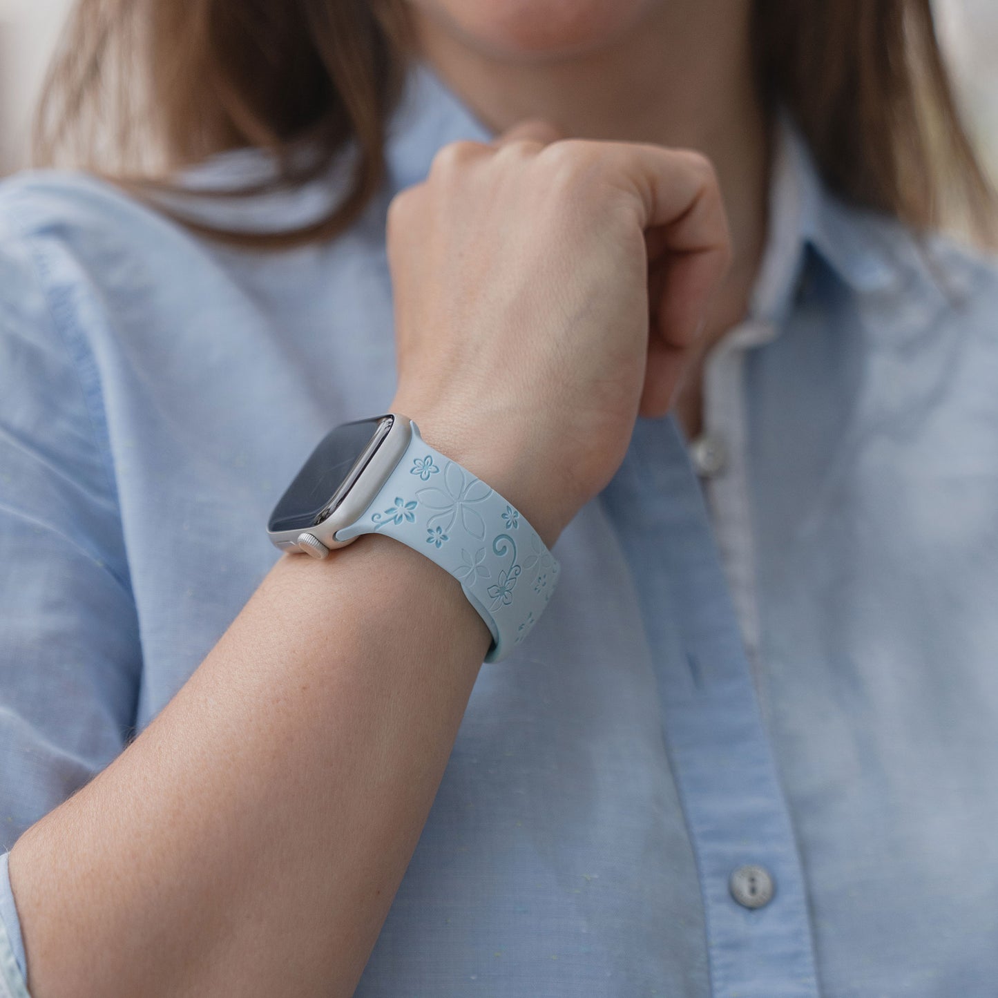 Eine Frau trägt das Arktisband Apple Watch Silikonarmband "Bloom" mit Blumenmuster, gepaart mit einem hellblauen Hemd.