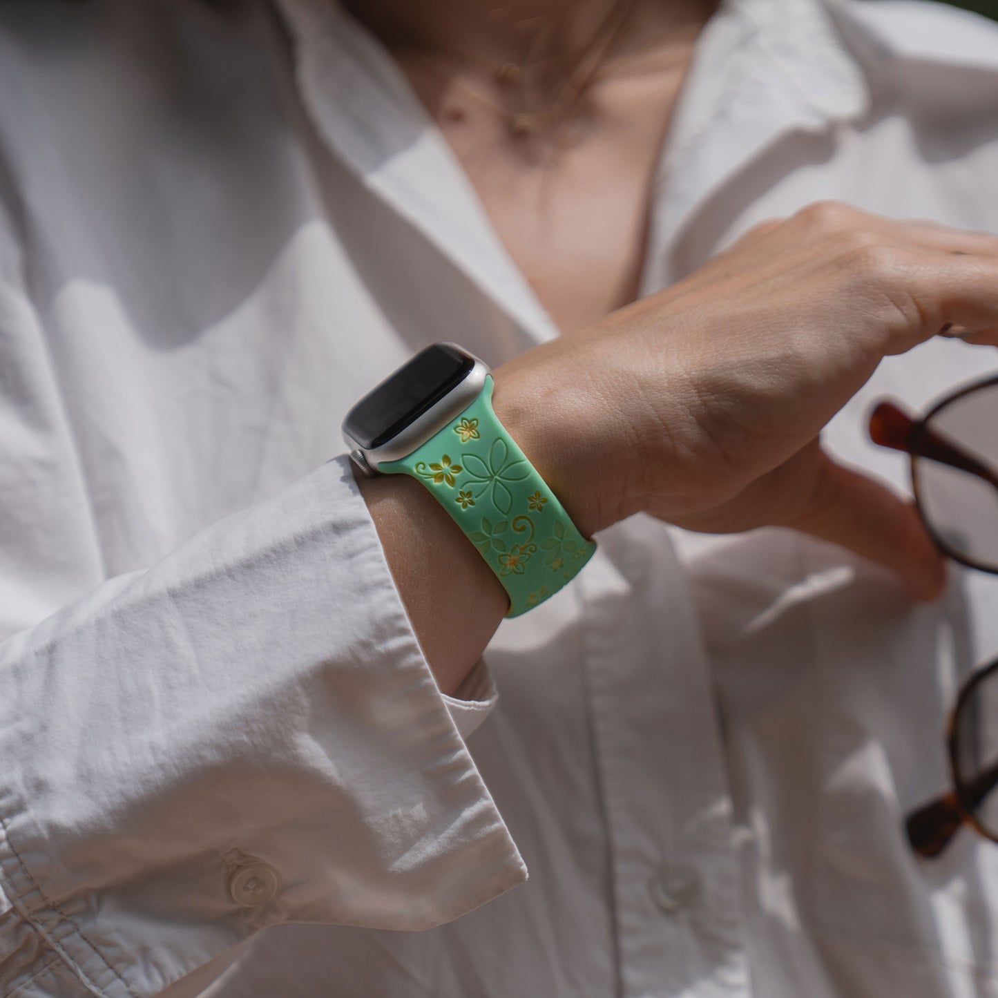 Eine Person trägt das arktisband Apple Watch Silikonarmband "Bloom" von arktisband im floralen Design, hält eine Brille und ist in ein weißes Hemd gekleidet.