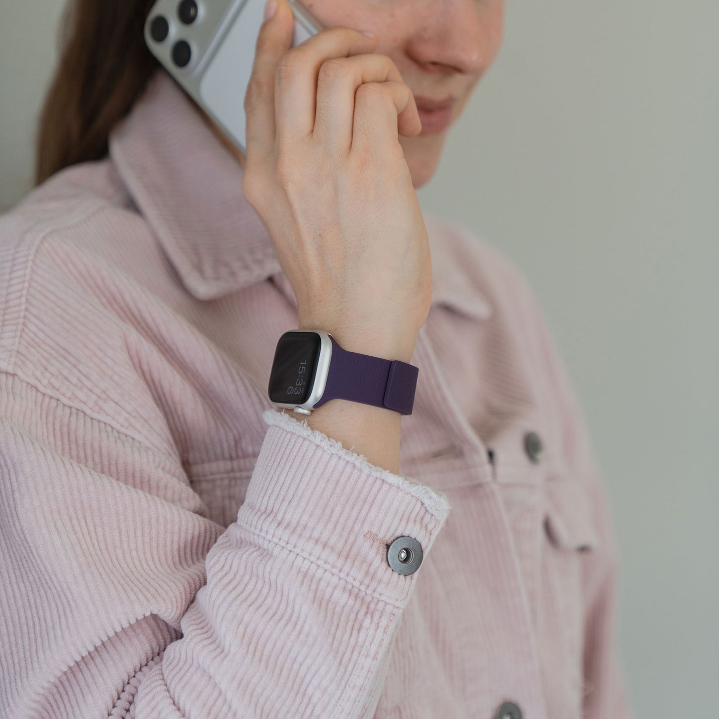 Eine Frau in einer rosa Jacke telefoniert, sie trägt das Arktisband Apple Watch magnetisches Silikonarmband "Flexy" mit einem lila, flexiblen Design an ihrem Handgelenk.
