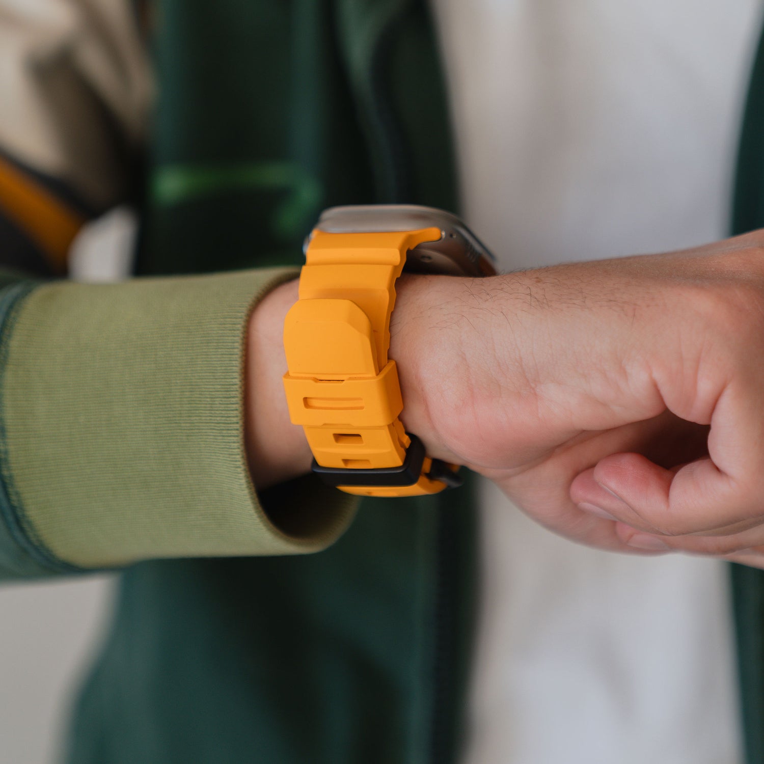 Jemand trägt ein arktisband Apple Watch Armband "Flux" in gelb mit Edelstahl Schließe von arktisband, gepaart mit einer grünen Jacke.