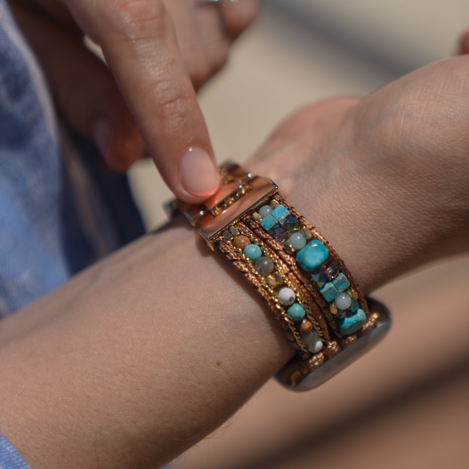 Eine Person legt sich ein „Sunset Spirit“-Armband von arktisband für die Apple Watch mit türkisfarbenen und braunen Perlen am Handgelenk an.