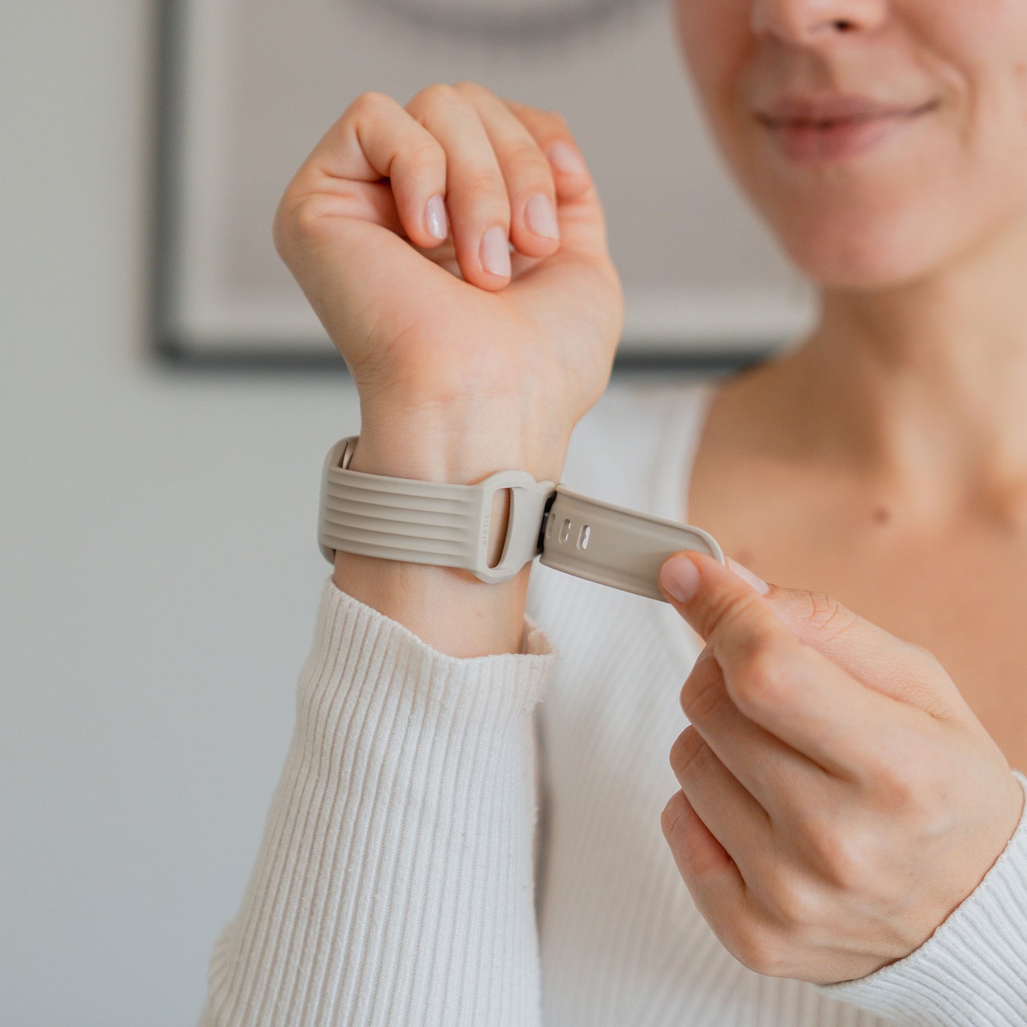 Eine Frau lächelt leicht, als sie sich ein arktisband Apple Watch Armband "Skandi" von arktisband in Beige um das Handgelenk legt.