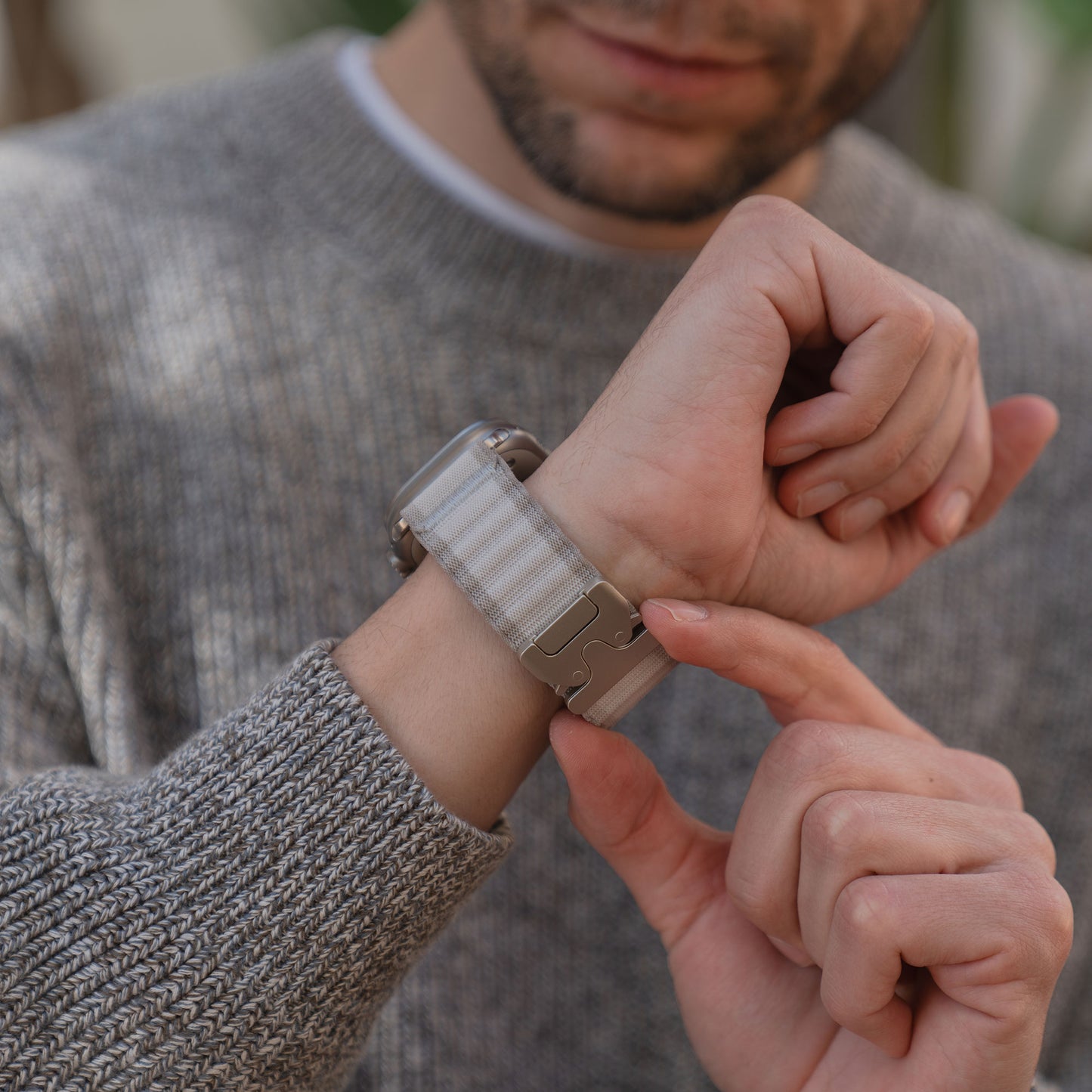 Mann, der den Parachute-Verschluss des Arktisband Apple Watch Armband "CoreX" an seinem Handgelenk anpasst, während er einen grauen Strickpullover trägt.