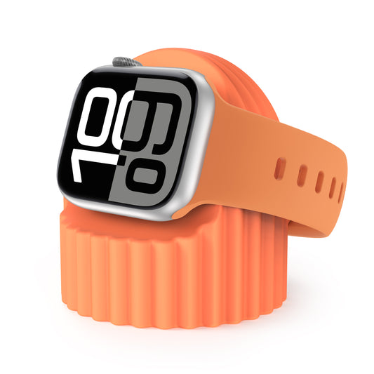 Eine Apple Watch mit orangefarbenem Armband liegt auf dem Arktis Apple Watch Silikon Dock „Luna“ und dient als Ladestation. Das Display zeigt deutliche digitale Zahlen auf weiß-schwarzem Hintergrund. Der gesamte Hintergrund ist weiß.