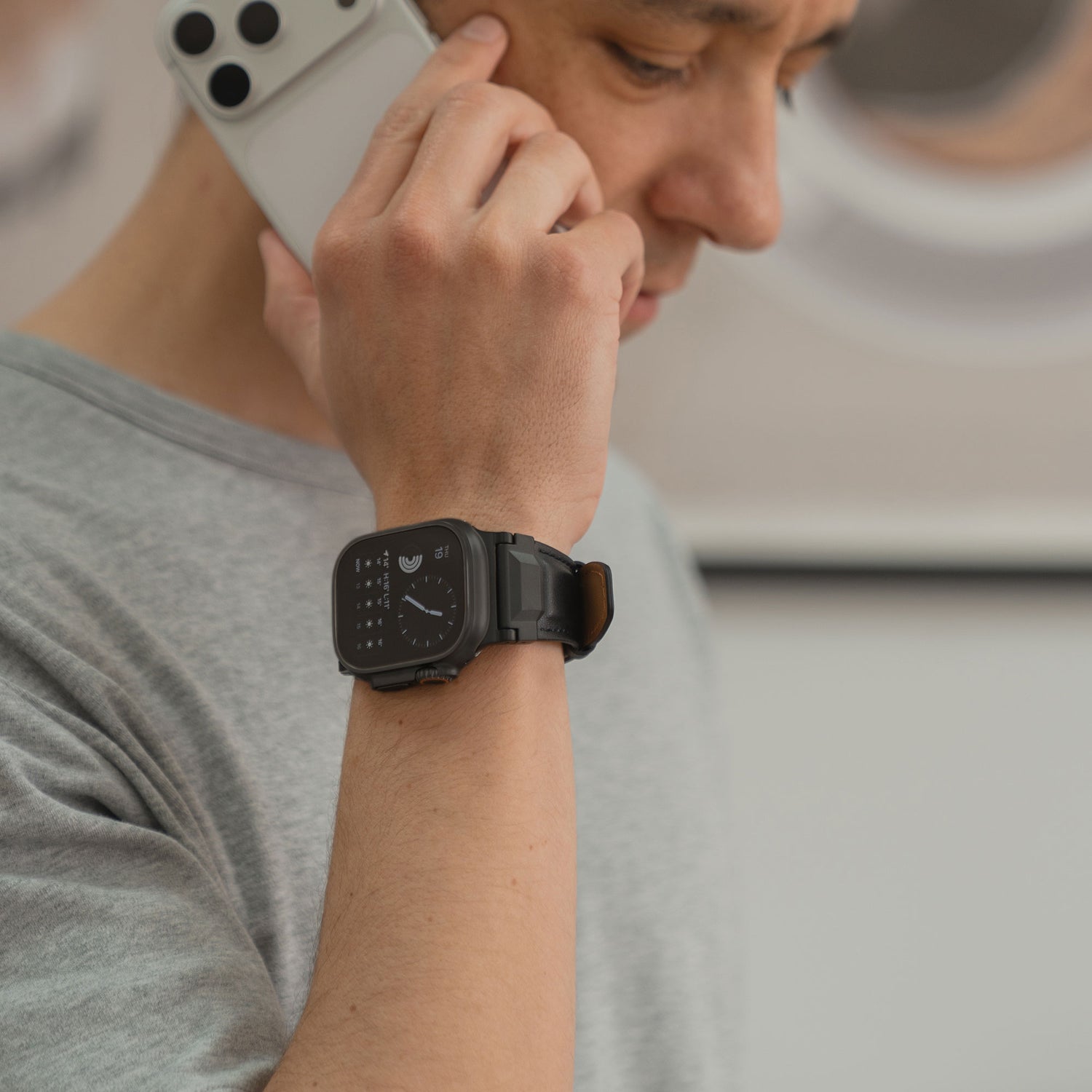Eine Person im grauen Hemd telefoniert mit einem Smartphone und trägt ein Arktisband Apple Watch Ultra Lederarmband "Delta" am Handgelenk.