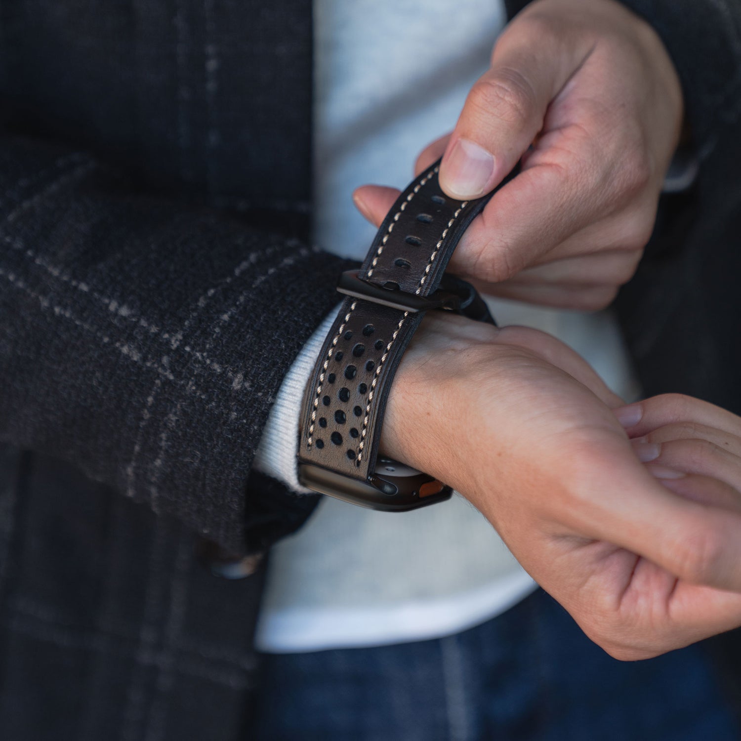 Nahaufnahme einer Person, die das arktisband Apple Watch Lederarmband "Toronto" - ein schwarzes perforiertes Lederarmband im klassischen Vintage-Design - um ihr Handgelenk legt.