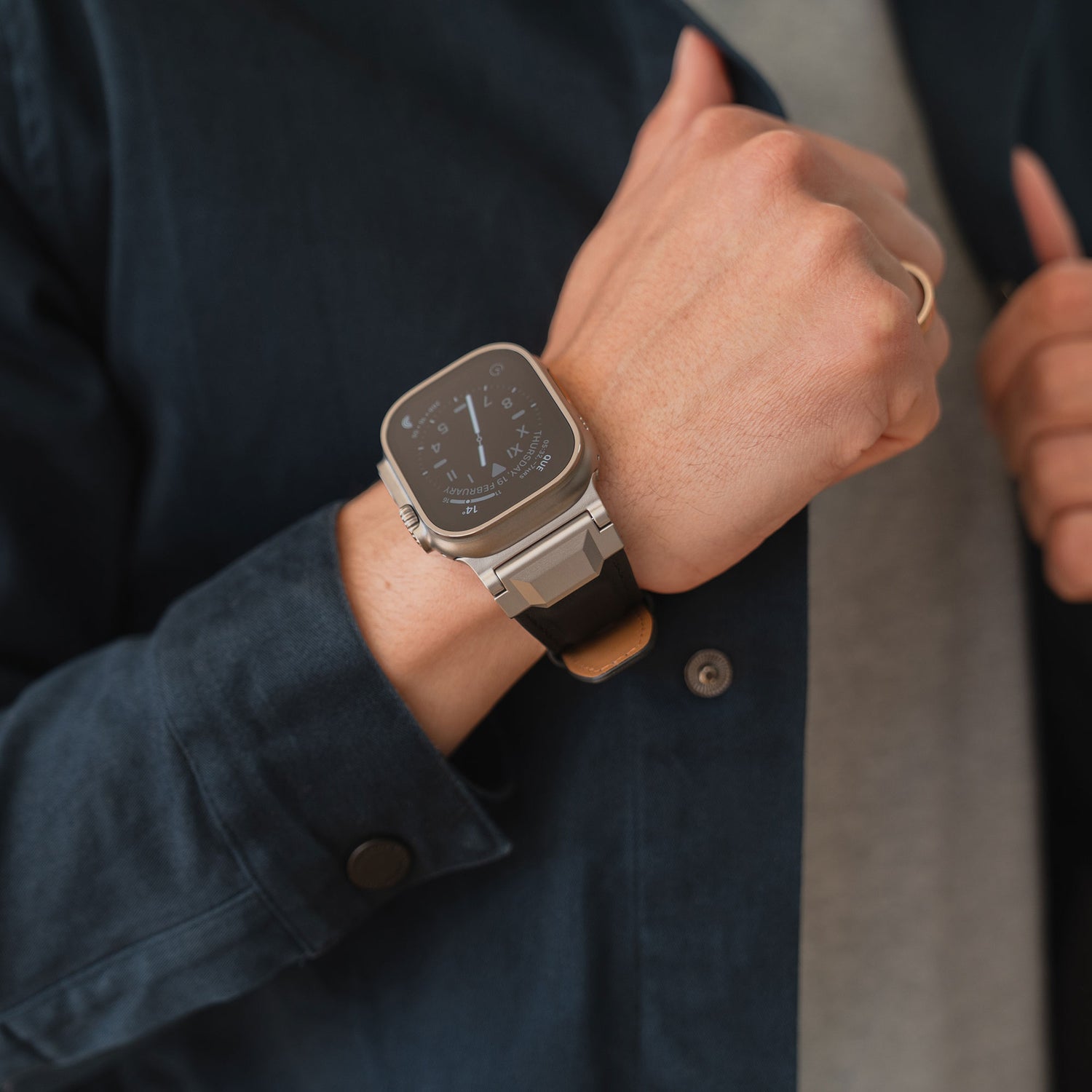 Eine Person trägt ein Arktisband Apple Watch Ultra Lederarmband "Delta" mit schwarzem Band und eine marineblaue Jacke, wobei sie den Ärmel verstellt.