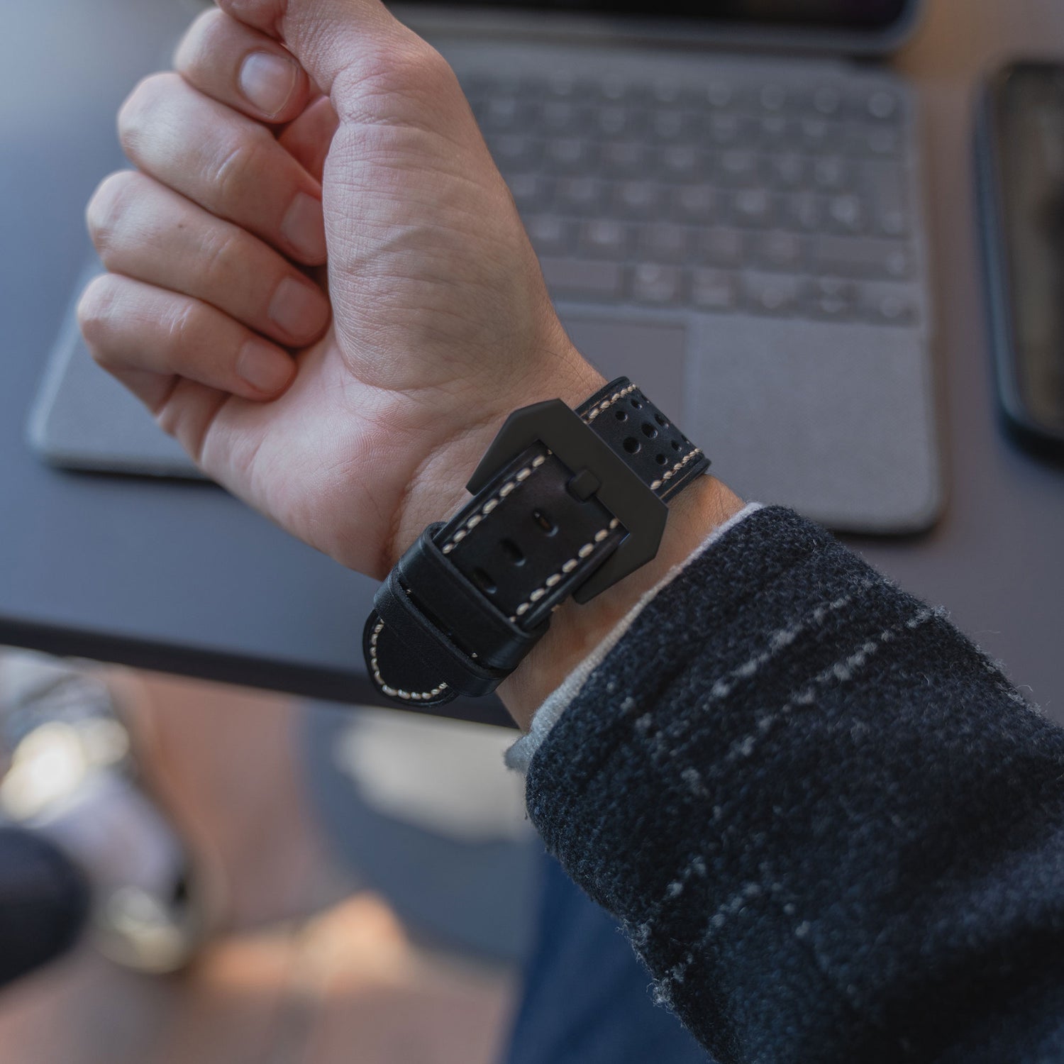 Das Handgelenk einer Person, die ein Arktisband Apple Watch Lederarmband "Toronto" in Schwarz mit weißen Nähten trägt, in der Nähe einer Laptop-Tastatur.