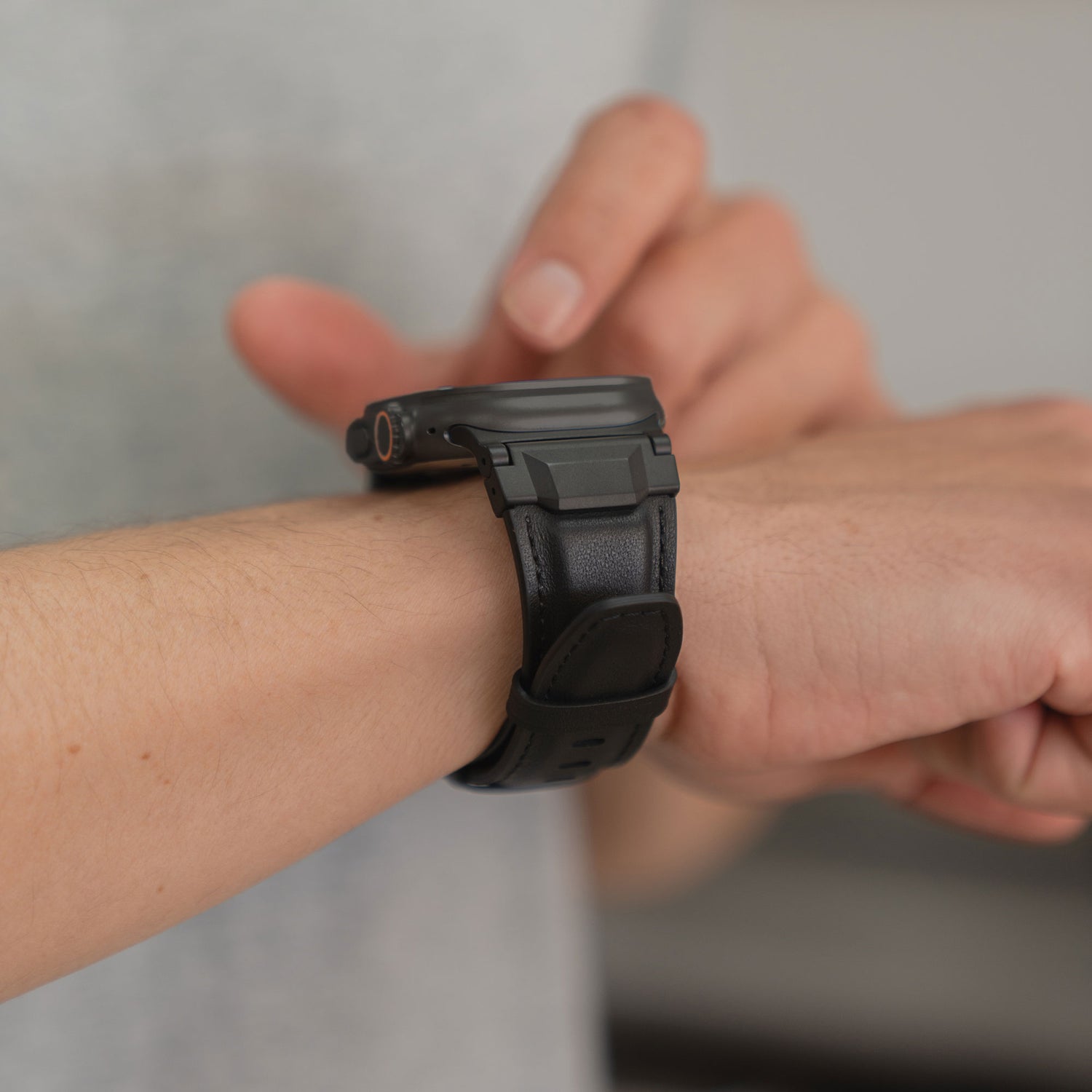 Nahaufnahme einer Person, die auf den Bildschirm einer schwarzen arktisband Apple Watch Ultra Lederarmband "Delta" von arktisband tippt, getragen am linken Handgelenk.