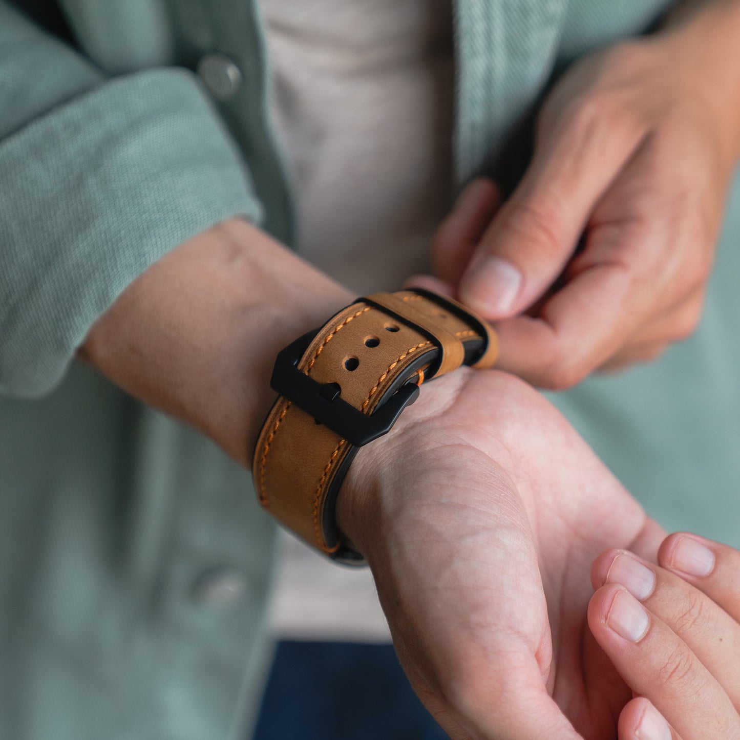 Nahaufnahme einer Person, die ein arktisband Apple Watch Ultra PALERMO GRANDE Lederarmband an ihrem Handgelenk befestigt, wobei die 316L-Edelstahlschließe von arktisband einen Hauch von Eleganz verleiht.