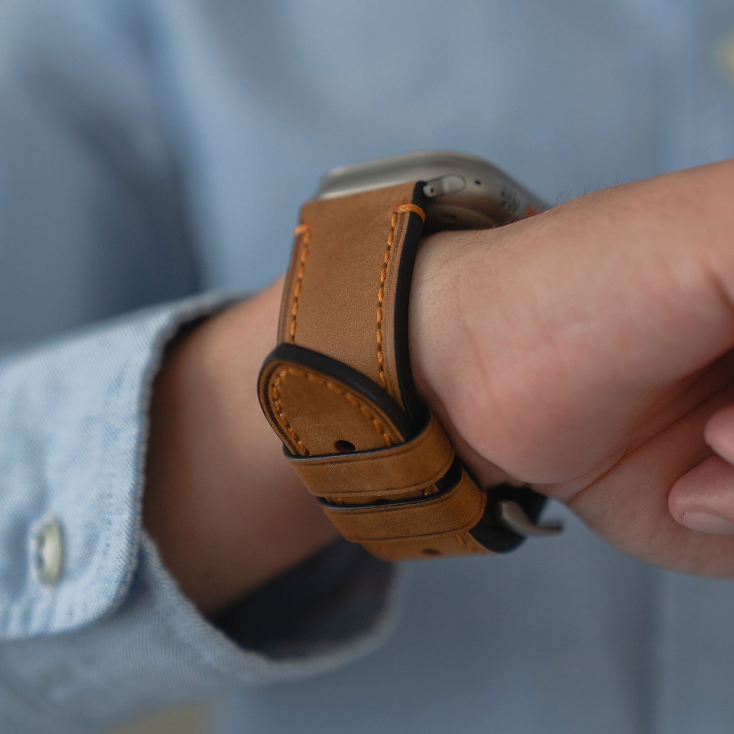 Nahaufnahme eines Handgelenks, das das Arktisband Apple Watch Ultra PALERMO GRANDE Lederarmband mit einer Schließe aus 316L-Edelstahl trägt, gepaart mit einem blauen Hemd.