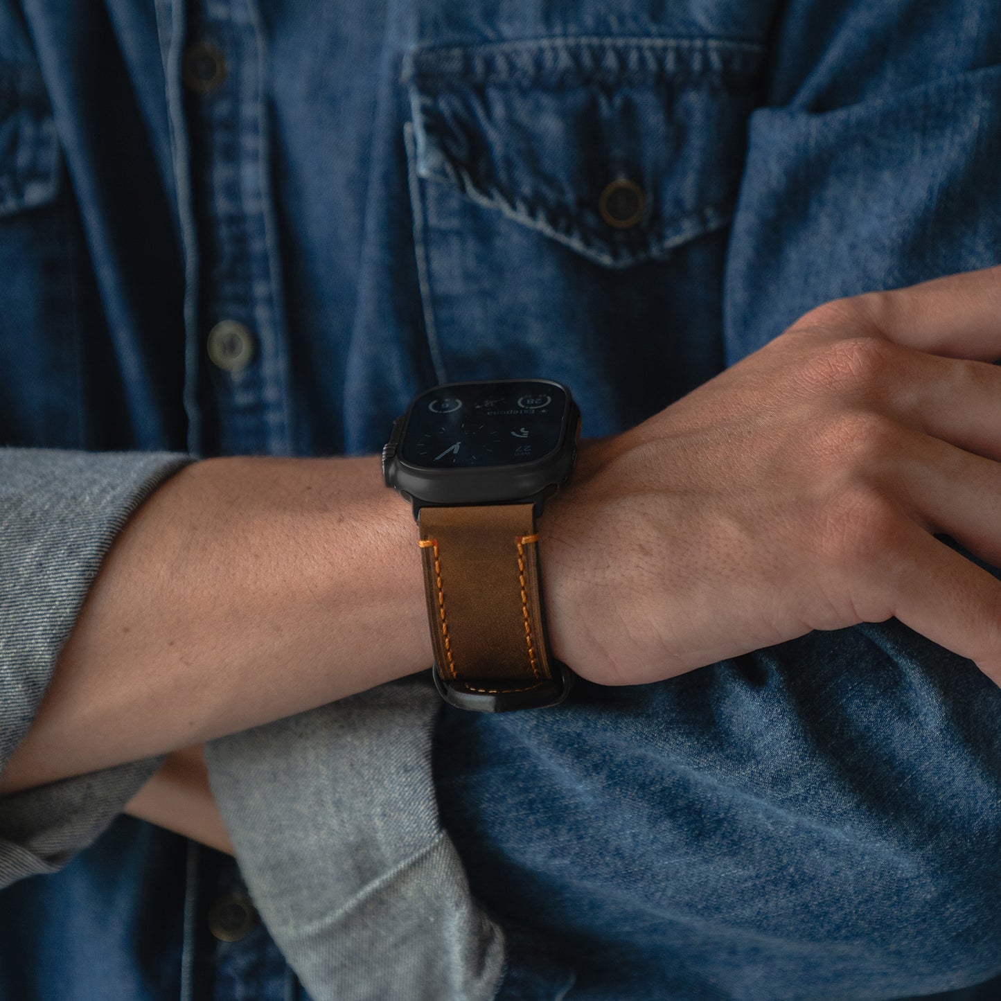 Person, die ein Arktisband Apple Watch Ultra PALERMO GRANDE Lederarmband mit einem blauen Jeanshemd und verschränkten Armen trägt.