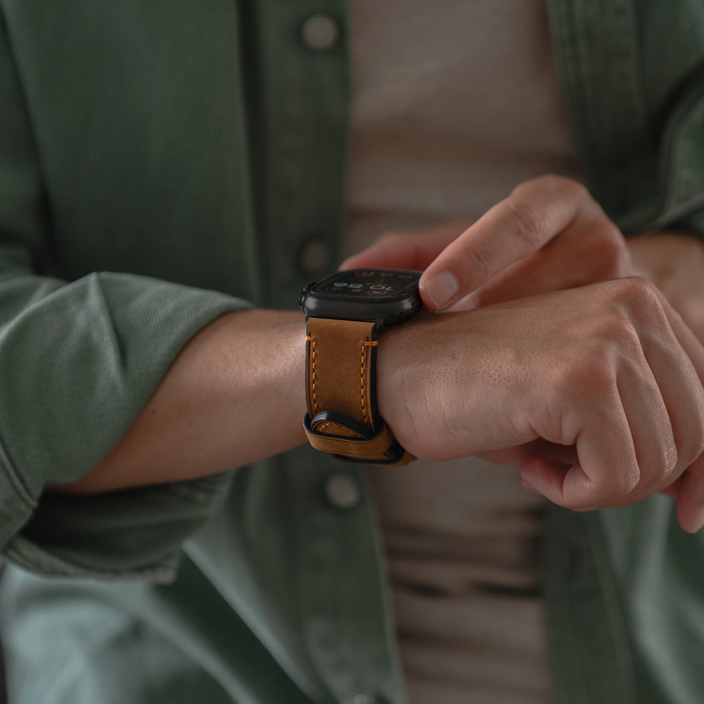 Eine Person in einem grünen Hemd passt ein Arktisband Apple Watch Ultra PALERMO GRANDE Lederarmband mit einer robusten 316L-Edelstahlschließe an ihr Handgelenk an.