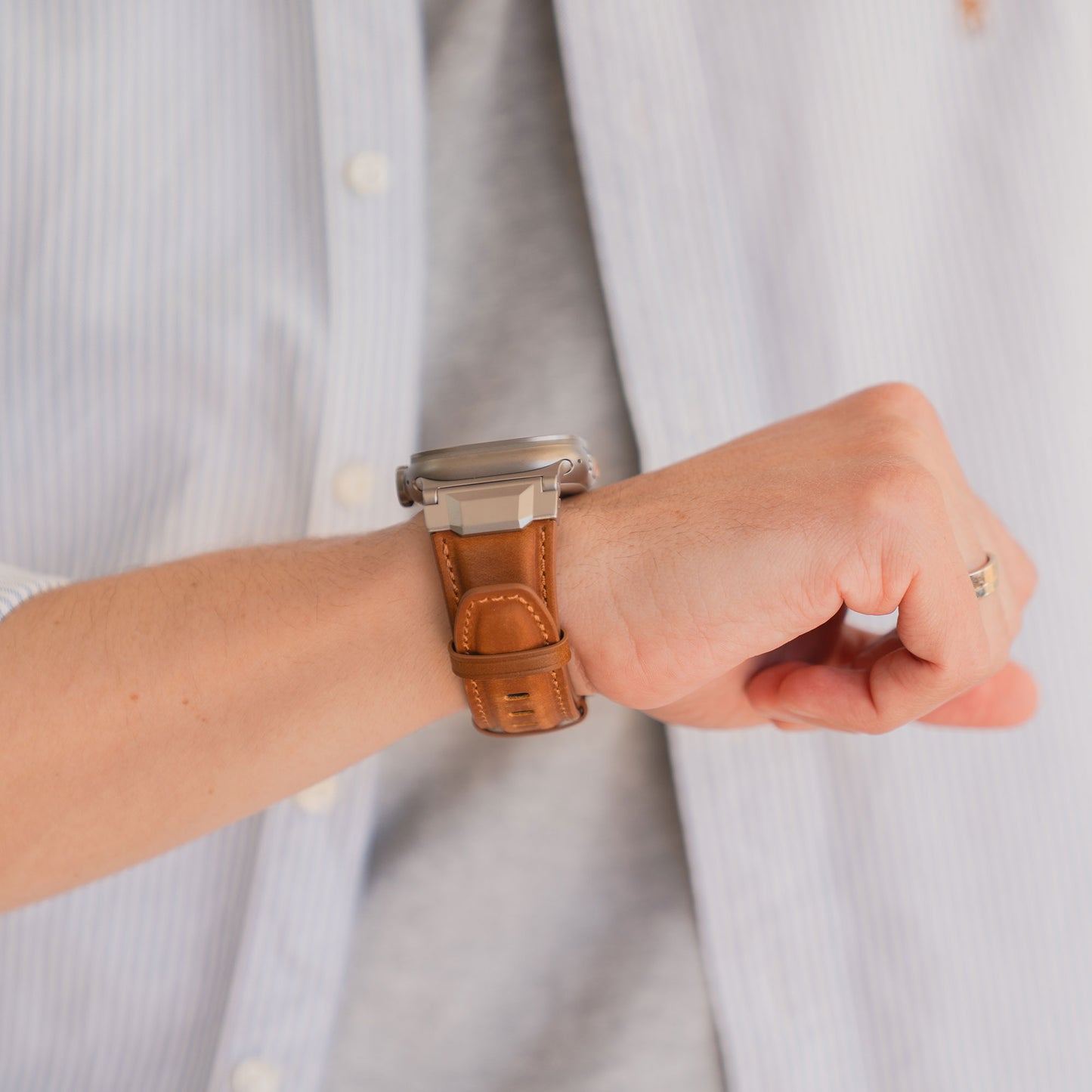 Eine Person, die das Arktisband Apple Watch Ultra Lederarmband "Delta" an ihrem Handgelenk trägt, bekleidet mit einem hellblauen Hemd.