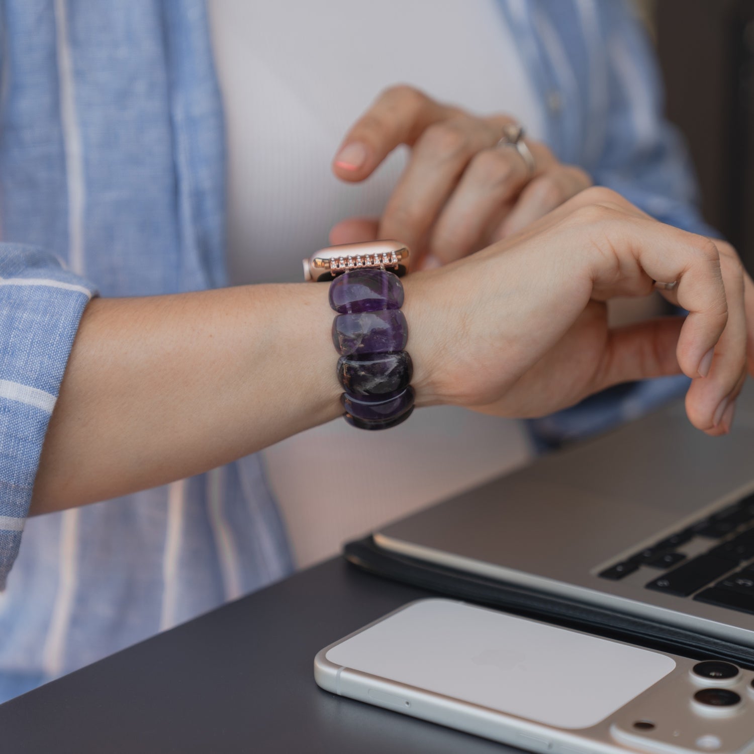 Eine Person, die ein Arktisband „Stone Pearl“ für die Apple Watch trägt und an einem Schreibtisch mit Laptop und Smartphone arbeitet.