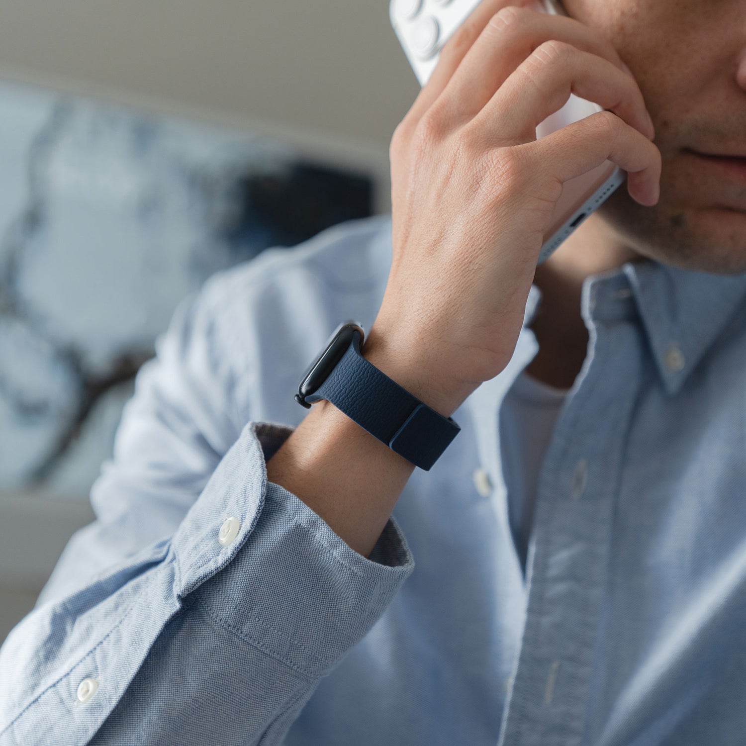 Ein Mann in einem blauen Hemd trägt ein Arktisband Apple Watch magnetisches Silikonarmband "Flexy" und hält ein Telefon an sein Ohr, wobei sein Gesicht teilweise sichtbar ist.