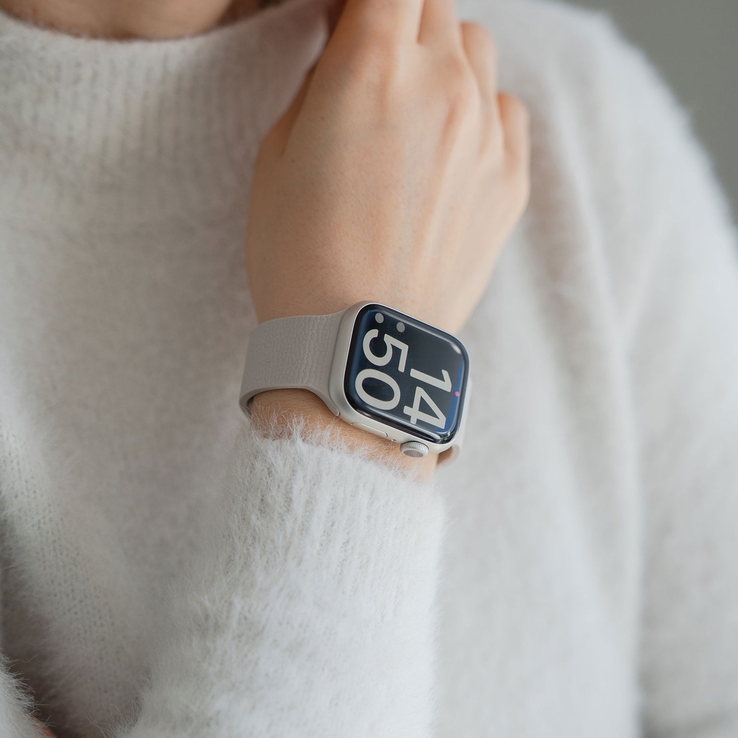 Eine Person, die das Arktisband Apple Watch magnetisches Silikonarmband "Flexy" mit Magnetverschluss an ihrem Handgelenk trägt, bekleidet mit einem flauschigen weißen Pullover.