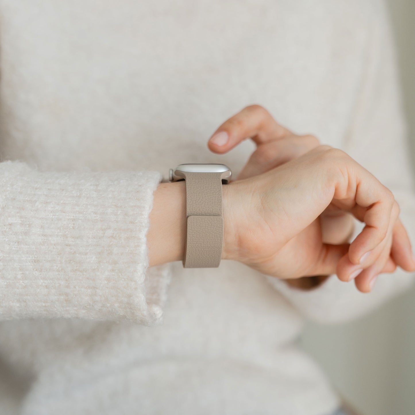 Person in einem cremefarbenen Pullover berührt eine beigefarbene Smartwatch mit dem arktisband Apple Watch magnetisches Silikonarmband "Flexy" von arktisband an ihrem Handgelenk.