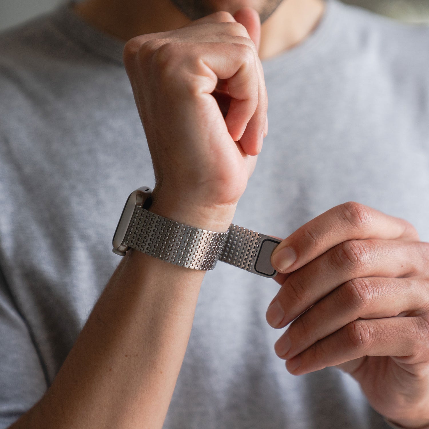 Eine Person, die ein Arktisband Apple Watch Edelstahlarmband „Aurora“ mit Magnetverschluss an ihrem Handgelenk befestigt und ein graues Hemd trägt.