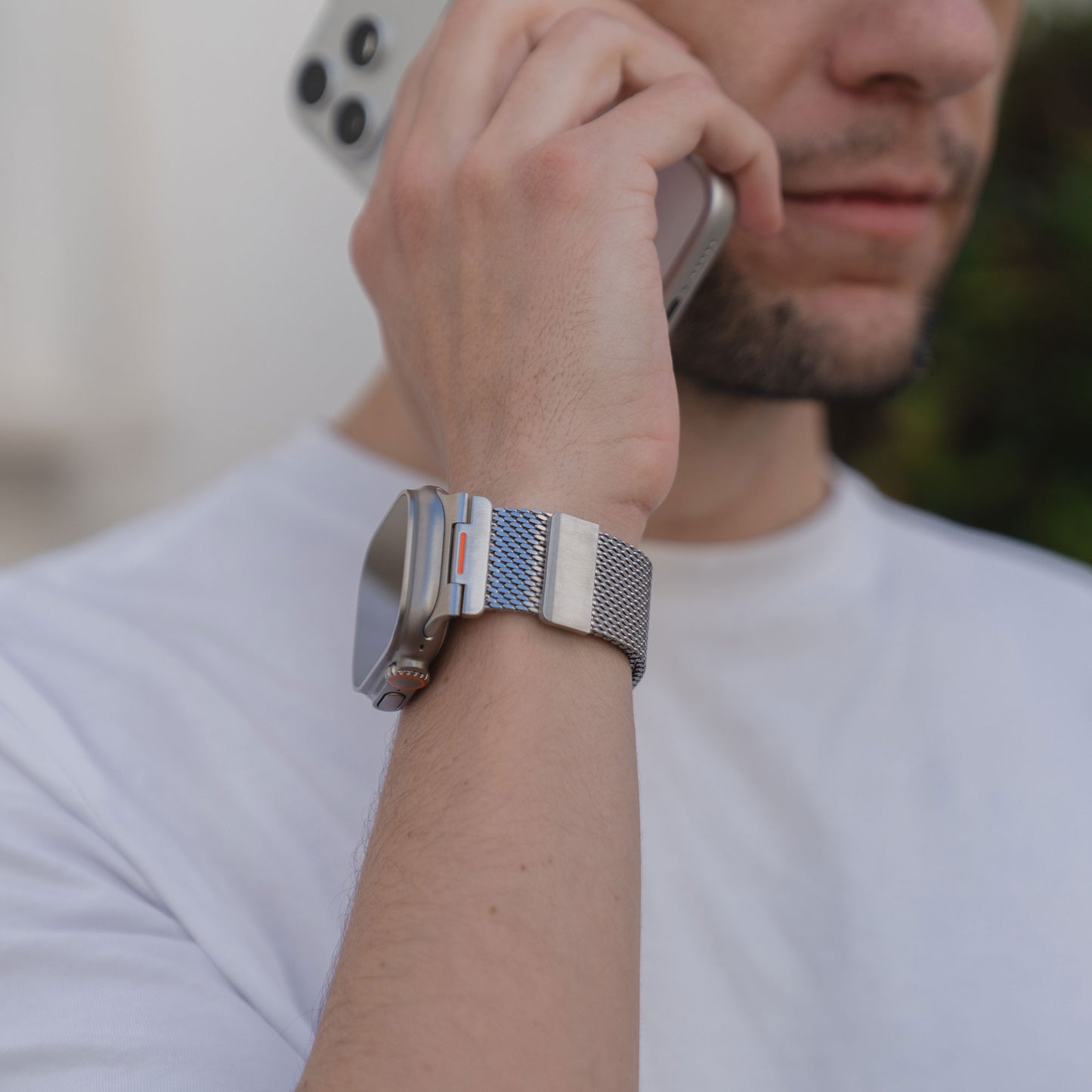 Ein Mann in weißem Hemd und Uhr hält sich ein Smartphone ans Ohr und präsentiert das arktisband Apple Watch Milanaise Armband "Bold SE" von arktisband für einen stilvollen Touch.