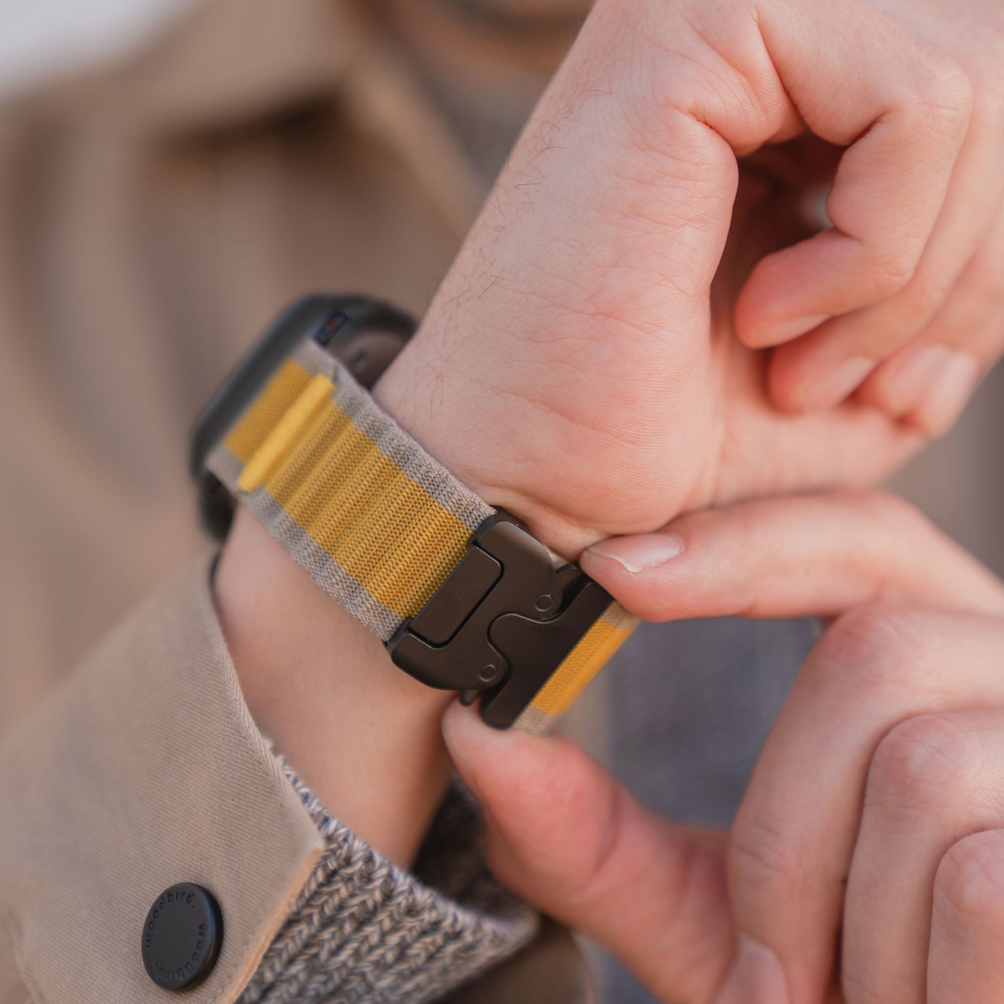 Nahaufnahme einer Person, die sich das arktisband Apple Watch Armband "CoreX" mit gelb-grau gestreiftem Stoffband und Parachute-Verschluss von arktisband um das Handgelenk legt.