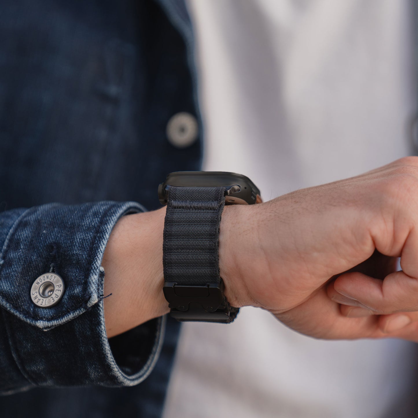 Jemand, der das arktisband Apple Watch Armband "CoreX" mit einem schwarzen Armband und einer Jeansjacke trägt und stilvoll die Zeit überprüft.