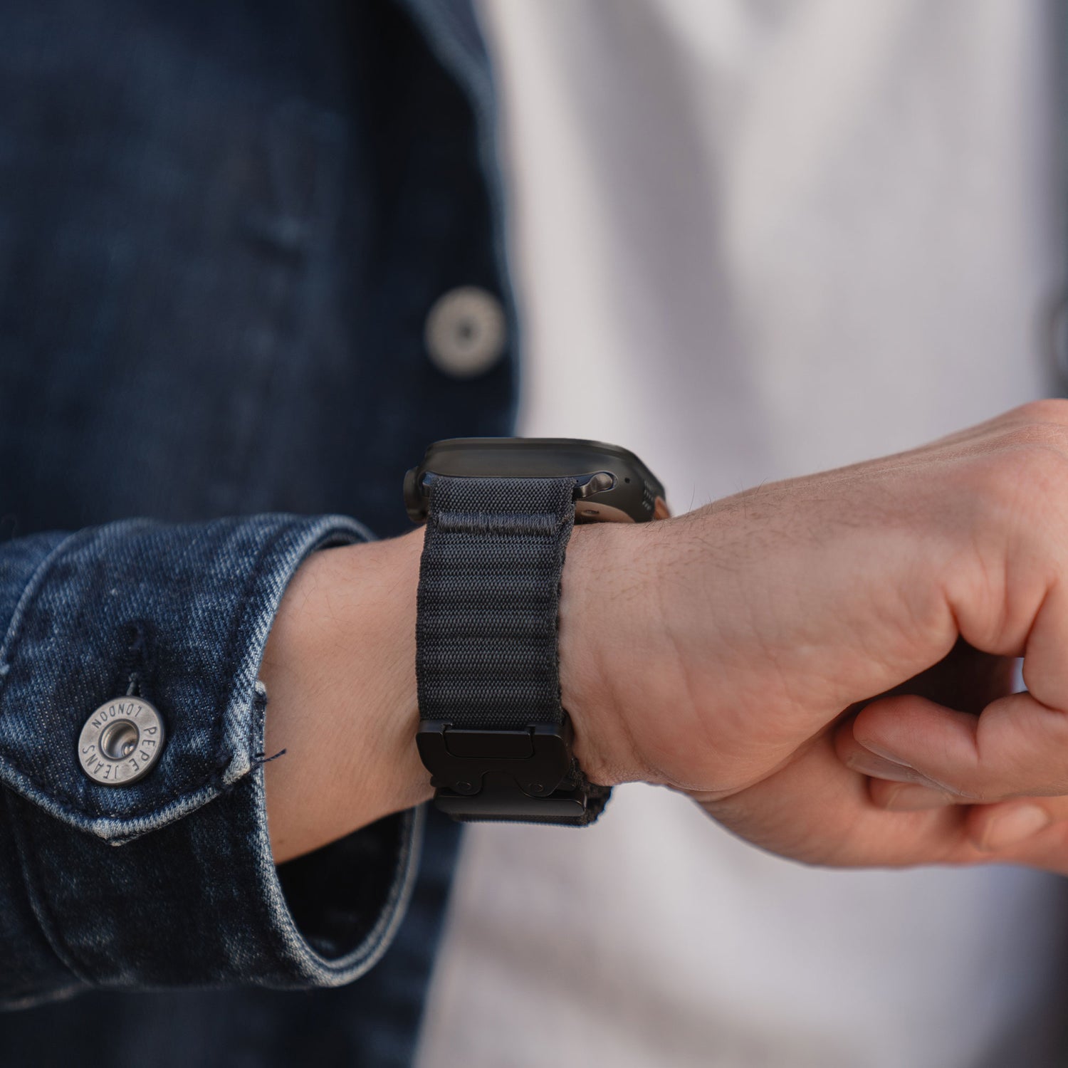 Jemand, der das arktisband Apple Watch Armband "CoreX" mit einem schwarzen Armband und einer Jeansjacke trägt und stilvoll die Zeit überprüft.