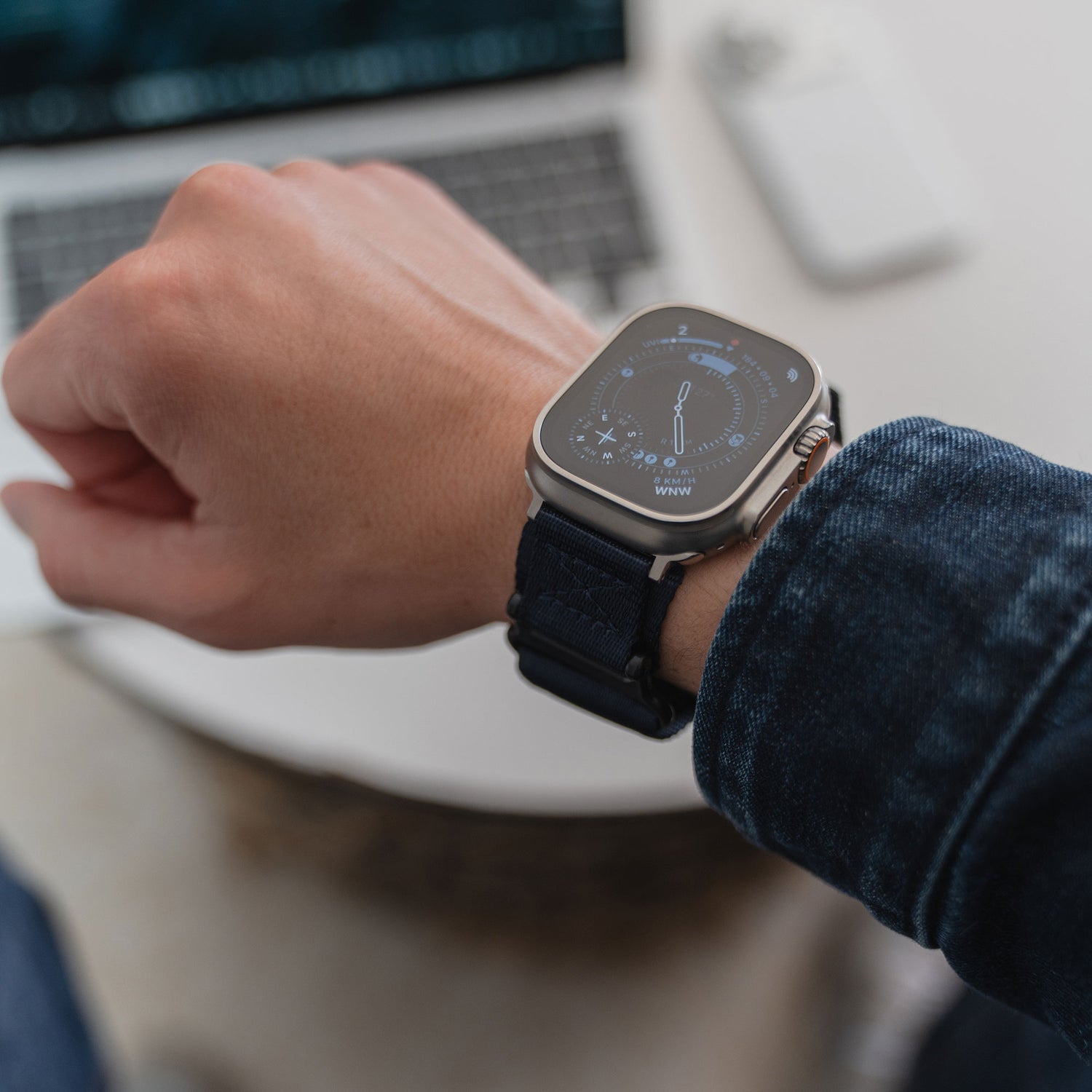 Eine Person, die das arktisband Apple Watch Outdoor Armband "Forge" von arktisband mit einem dunklen Nylonband trägt, sitzt neben einem Laptop und einer weißen drahtlosen Maus.