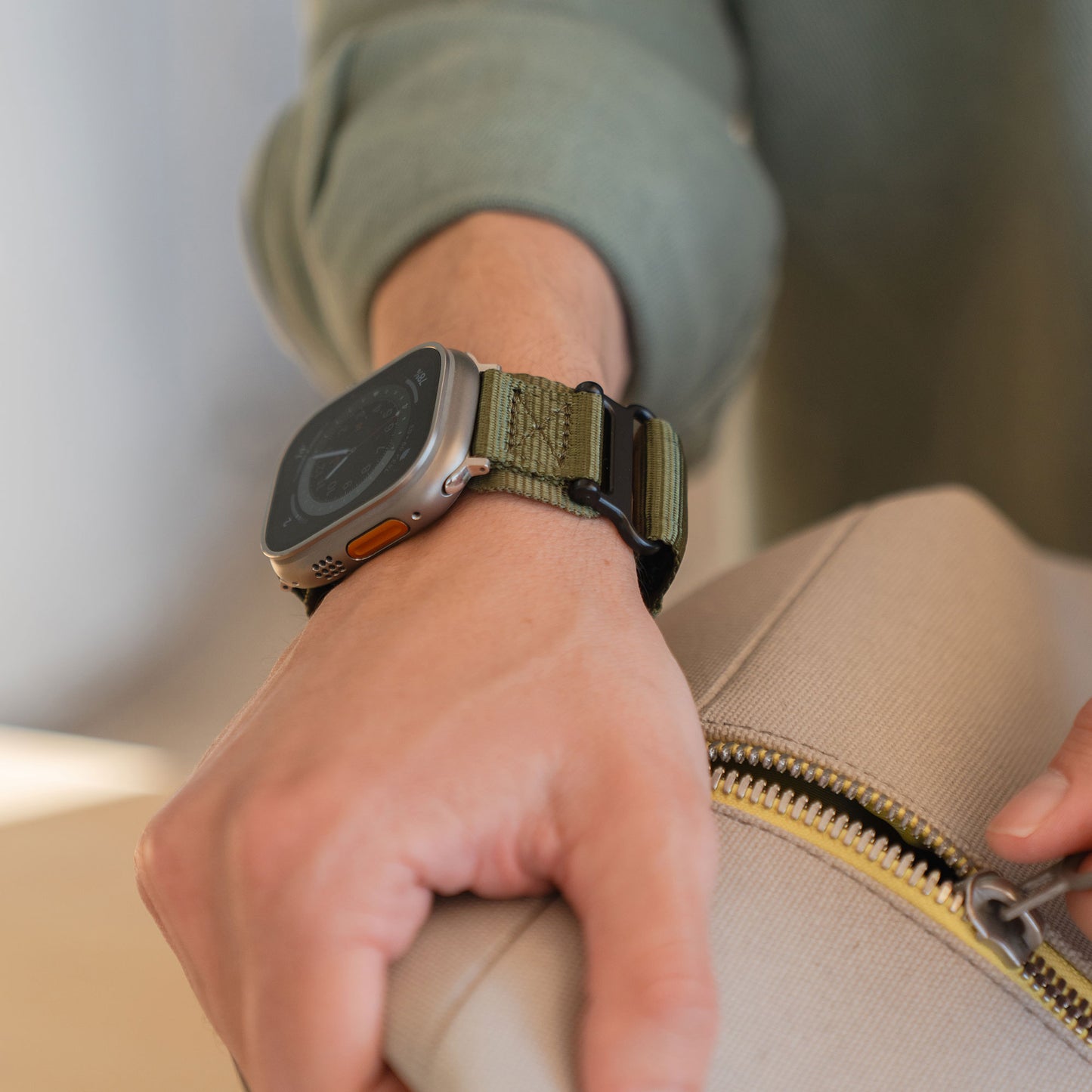 Eine Person, die das arktisband Apple Watch Outdoor Armband "Forge" mit grünem Band trägt, hält eine beige Tasche mit Reißverschluss.