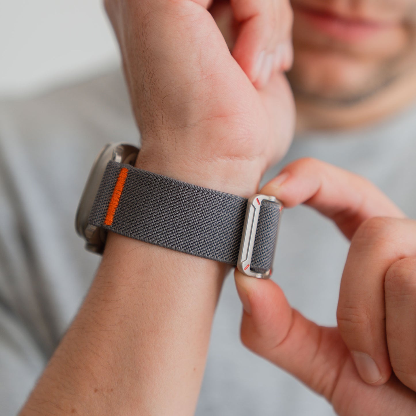 Eine Person befestigt das arktisband Apple Watch Nylonarmband "FlexOne" mit orangefarbenem Detail an ihrem Handgelenk und erreicht so einen perfekten Sitz für ihre Apple Watch.