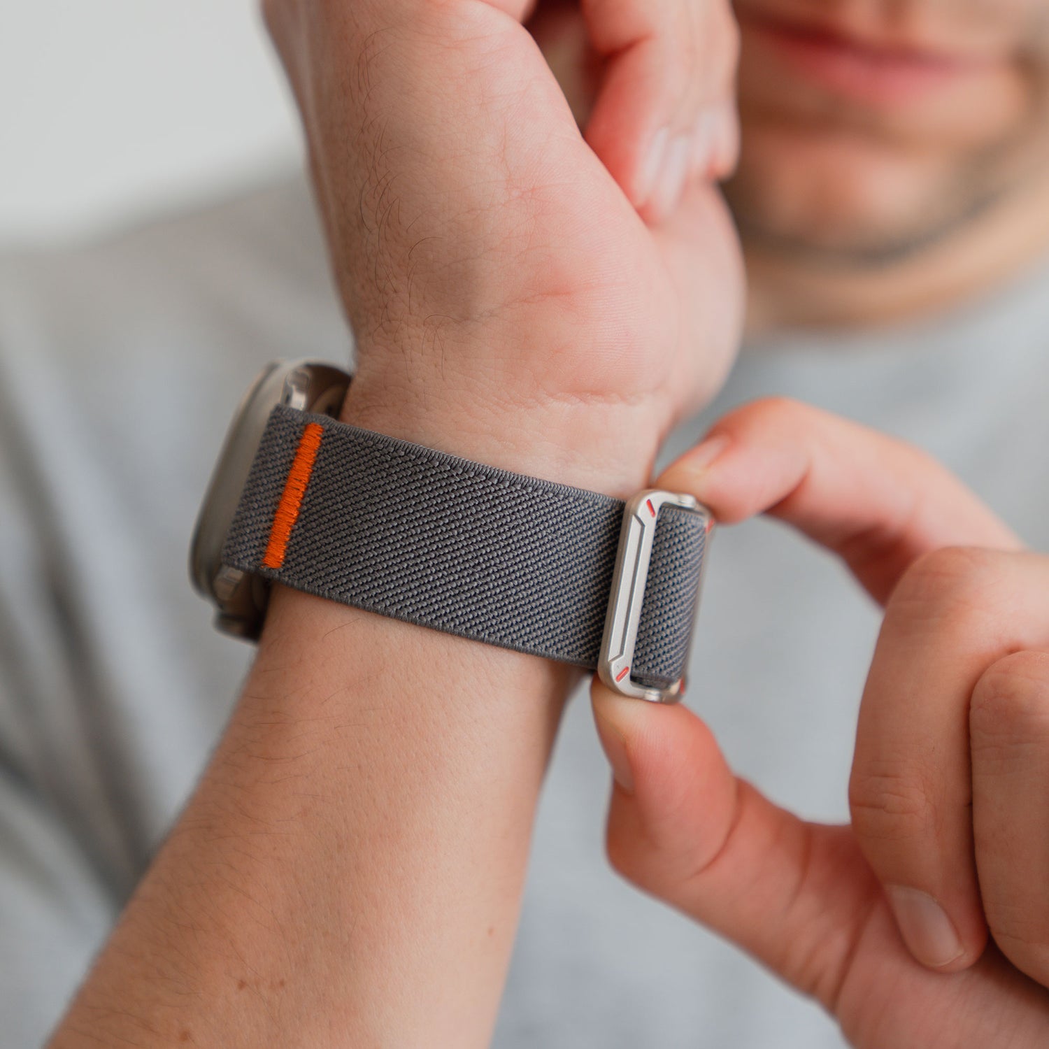 Eine Person befestigt das arktisband Apple Watch Nylonarmband "FlexOne" mit orangefarbenem Detail an ihrem Handgelenk und erreicht so einen perfekten Sitz für ihre Apple Watch.