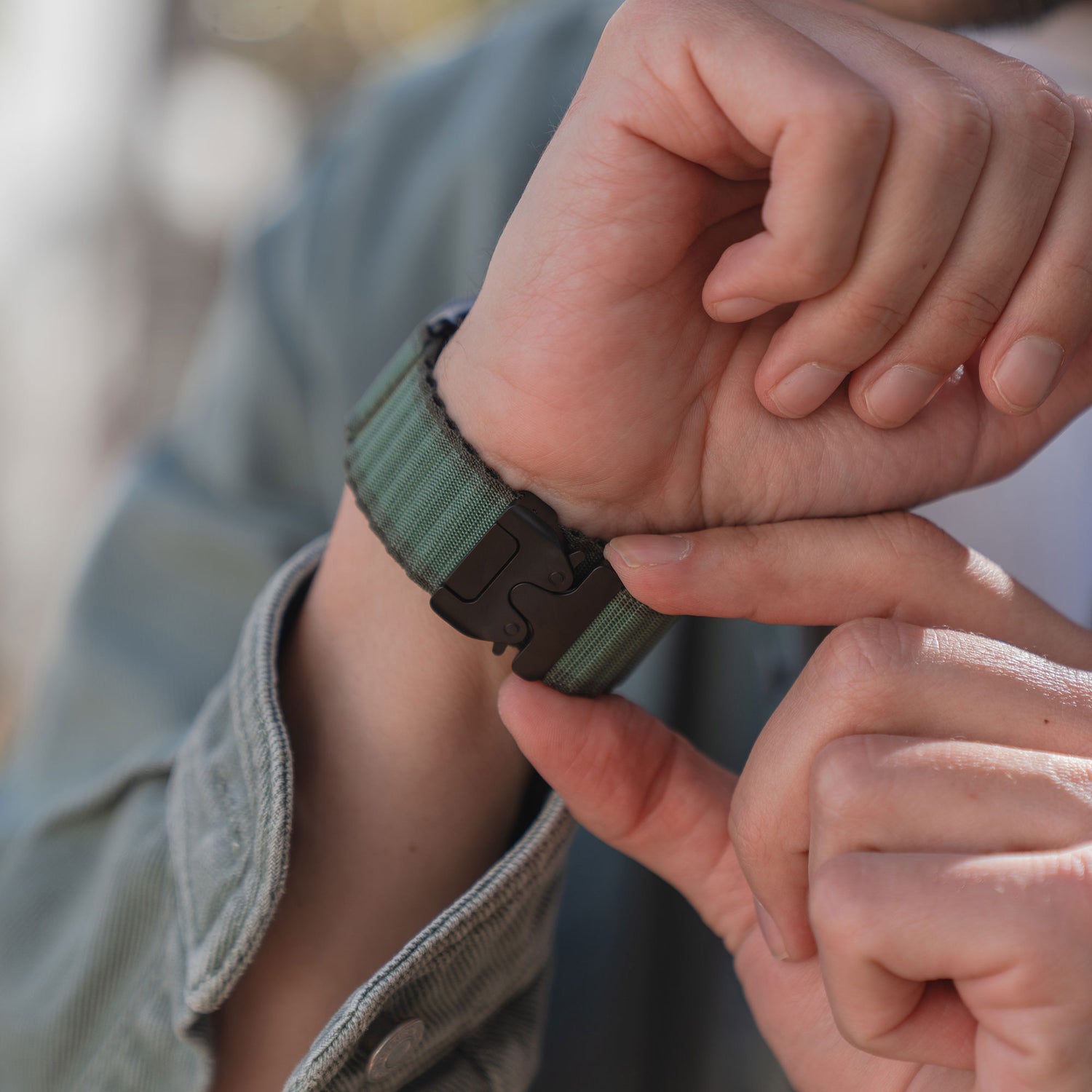 Eine Person befestigt das grüne Arktisband Apple Watch Armband "CoreX" mit einem Parachute-Verschluss und einer schwarzen Metallschließe an ihrem Handgelenk.