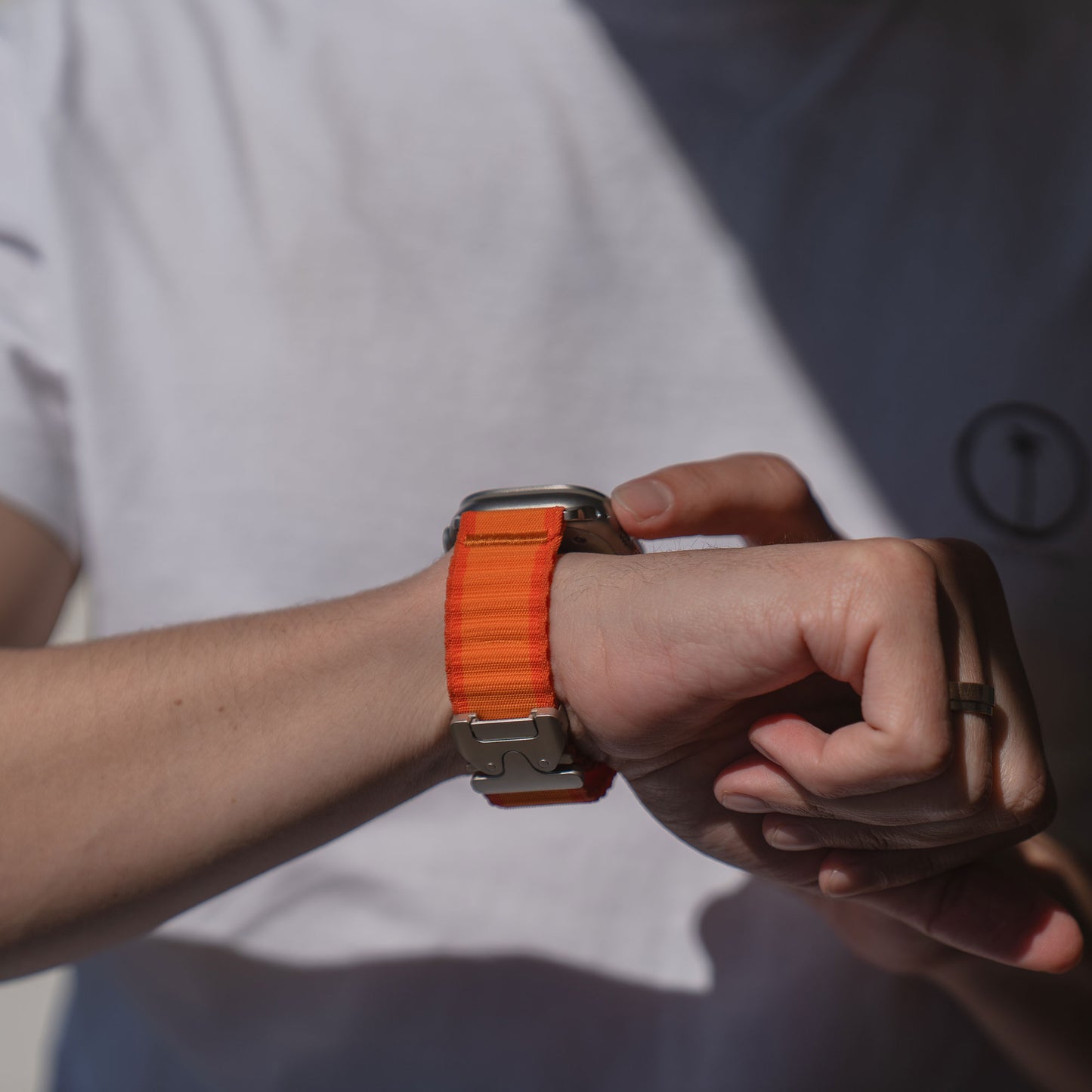 Eine Person in einem weißen Hemd passt das arktisband Apple Watch Armband "CoreX" mit einem orangefarbenen Band im Wave-Look an ihr Handgelenk an.