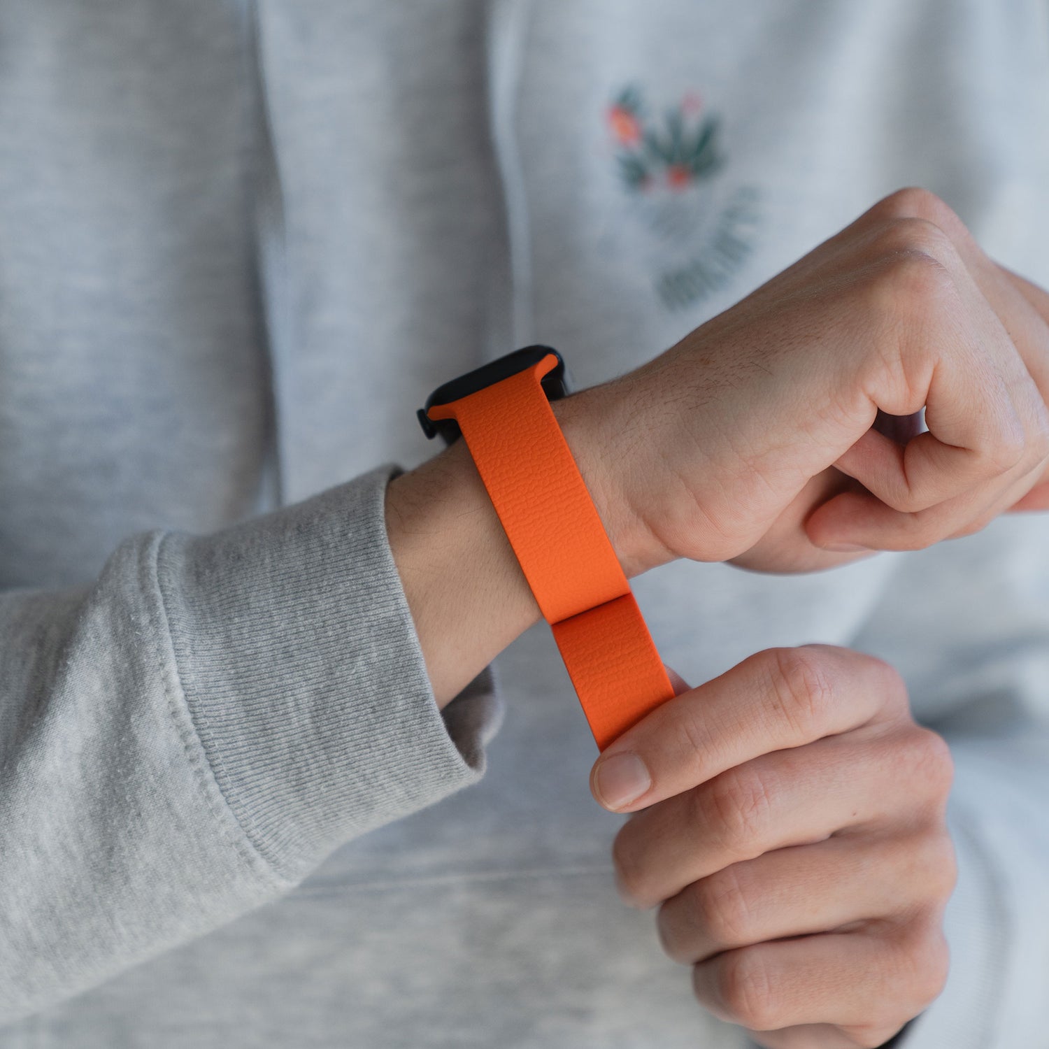Eine Person, die das Arktisband Apple Watch magnetisches Silikonarmband "Flexy" in orange trägt, stellt das flexible Arktisband an ihrem Handgelenk ein.